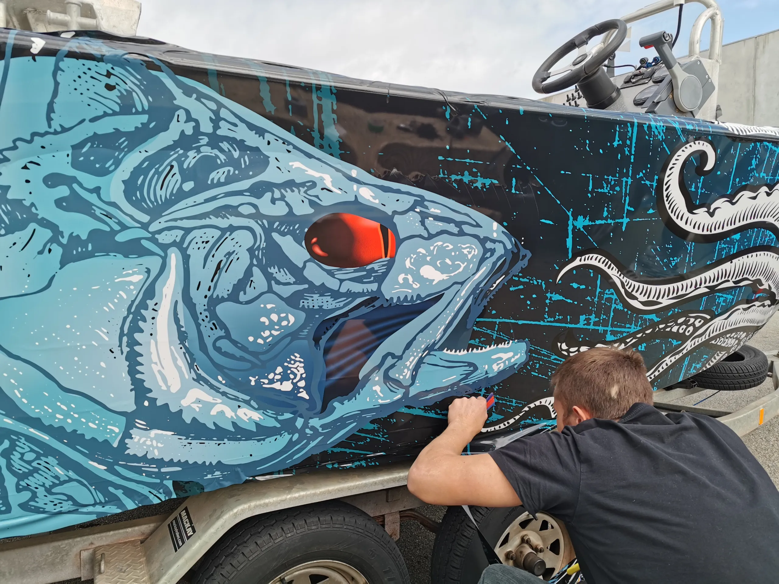 Installer seen from behind smoothing blue fish graphics onto the boat hull
