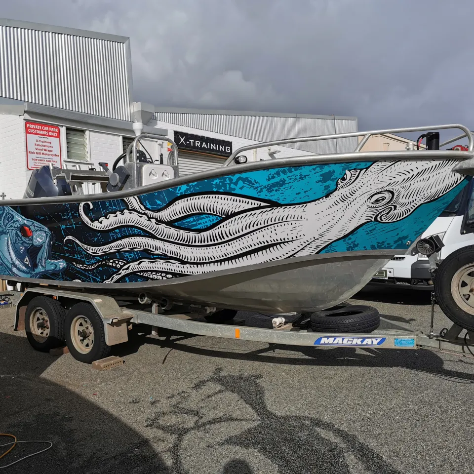 Boat on a trailer with white squid and blue fish artwork across its hull outside the workshop