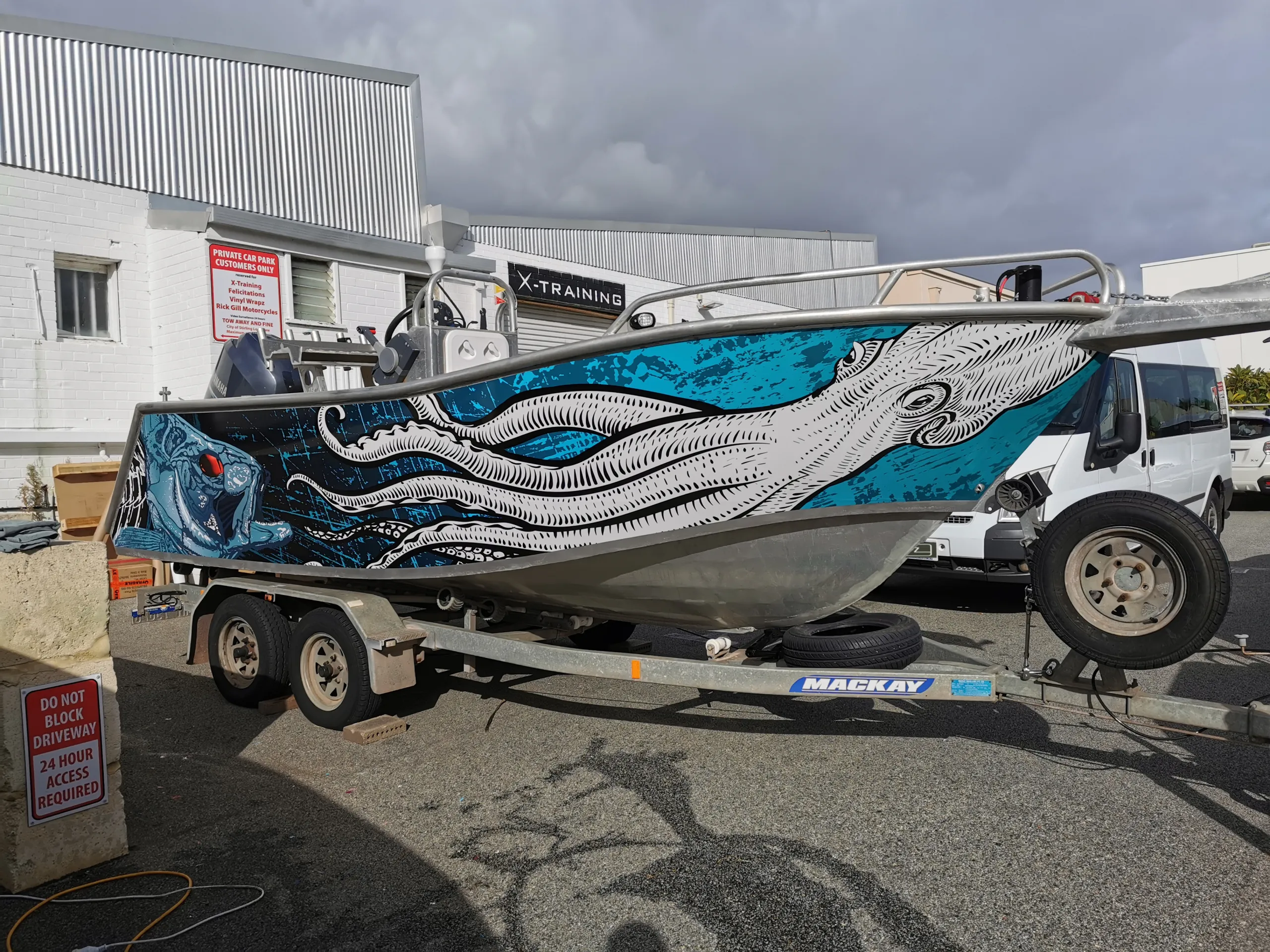 Boat on a trailer with white squid and blue fish artwork across its hull outside the workshop