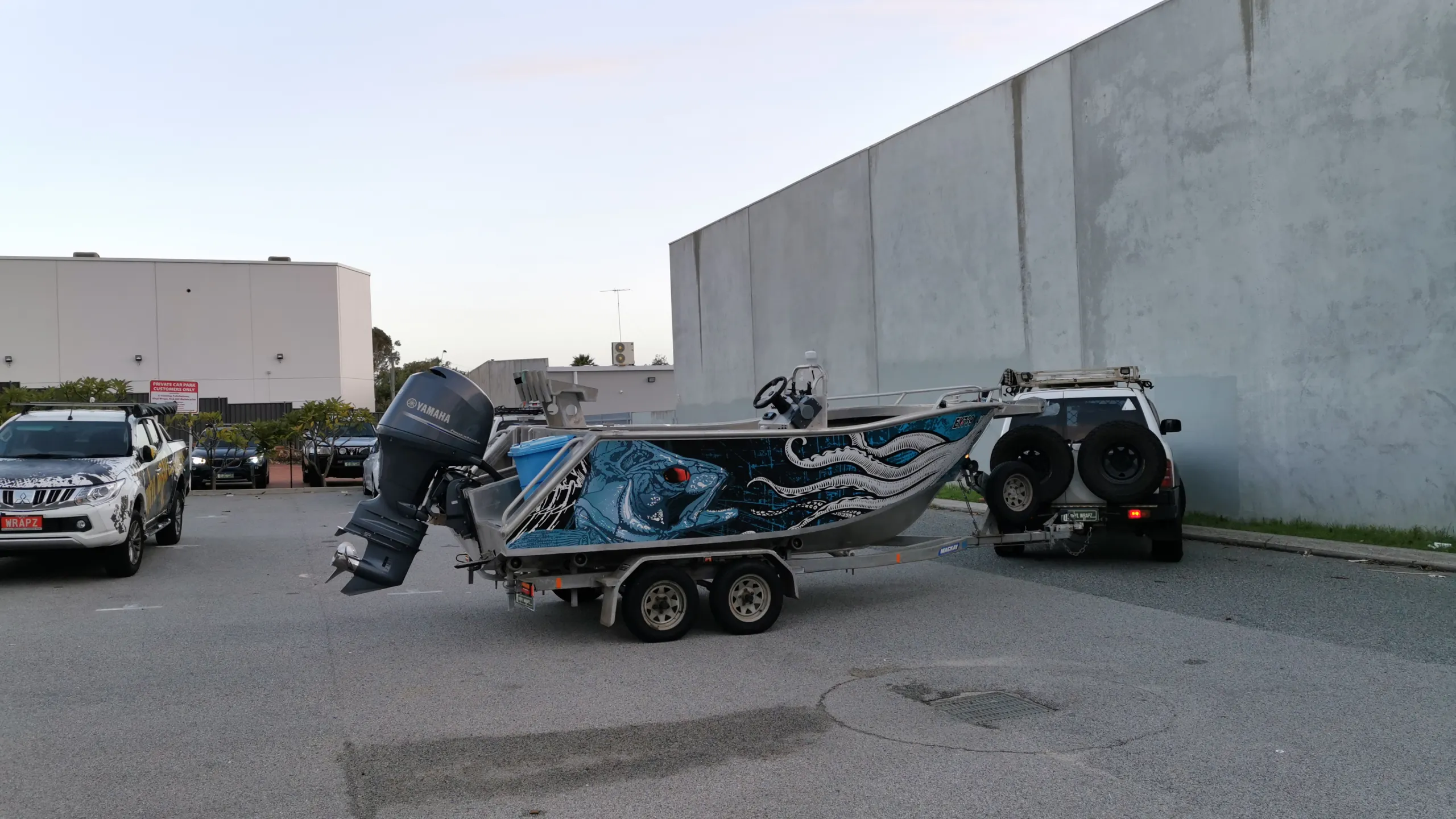 Wide view of a trailer boat with blue fish and white squid graphics beside its tow vehicle