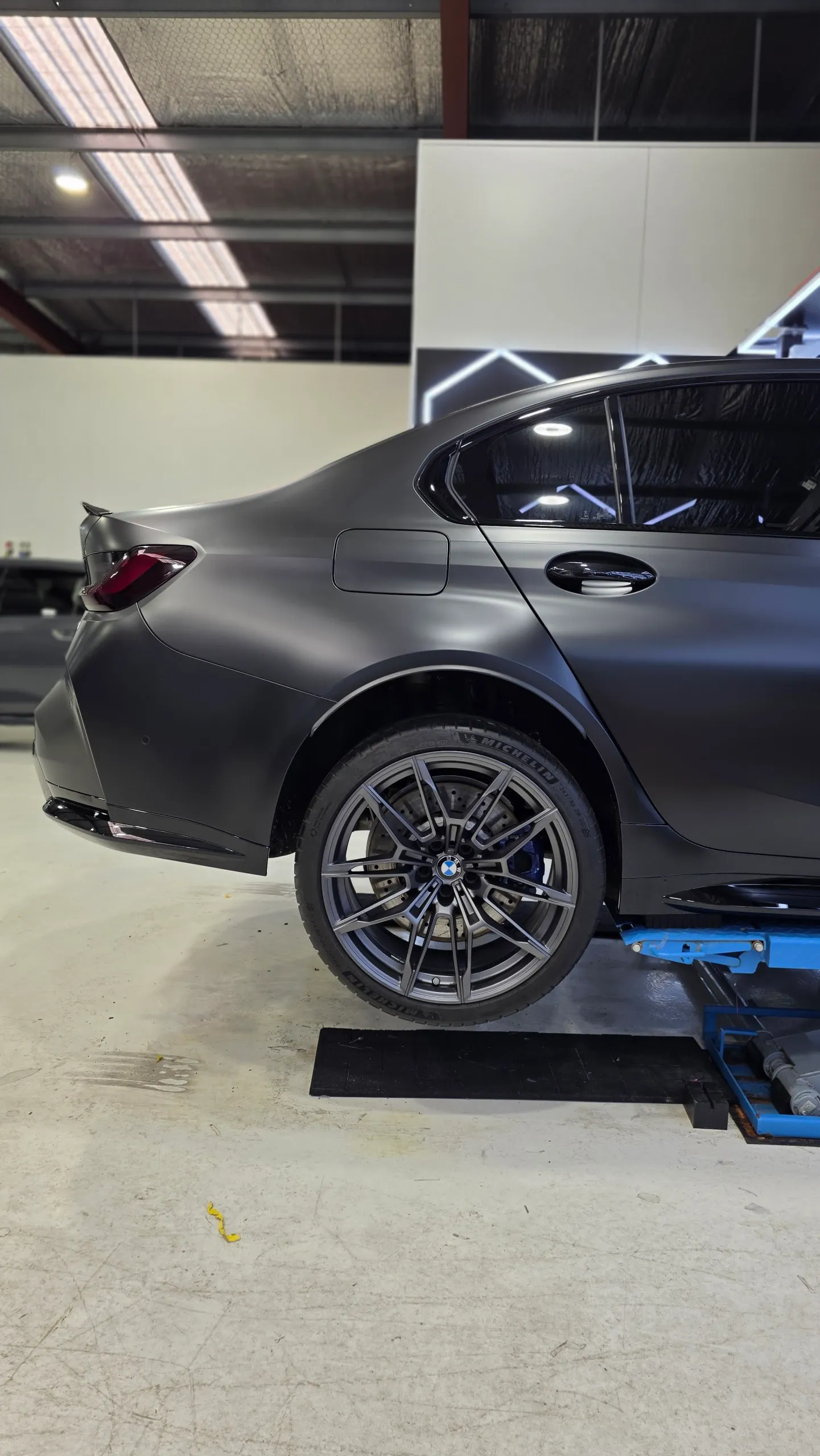 BMW M3 Competition rear wheel and satin dark grey quarter panel on a workshop lift