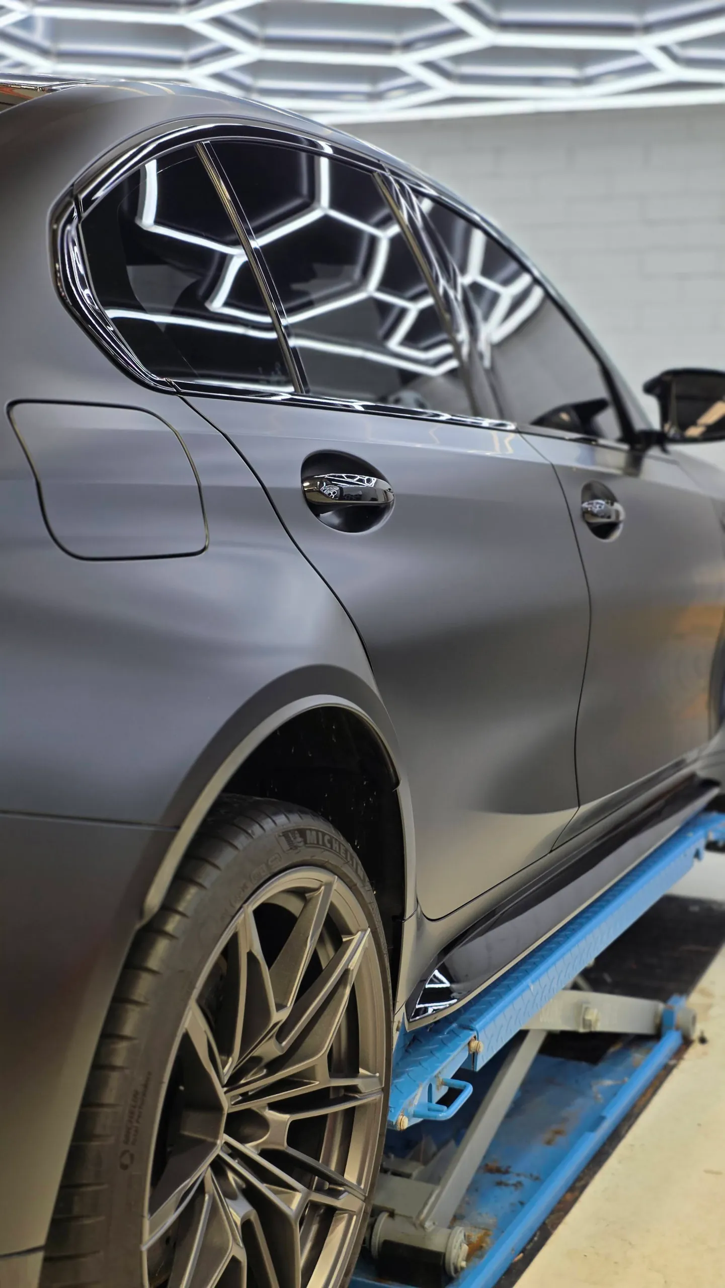 Satin grey BMW M3 Competition rear door, rear quarter and wheel on a workshop lift