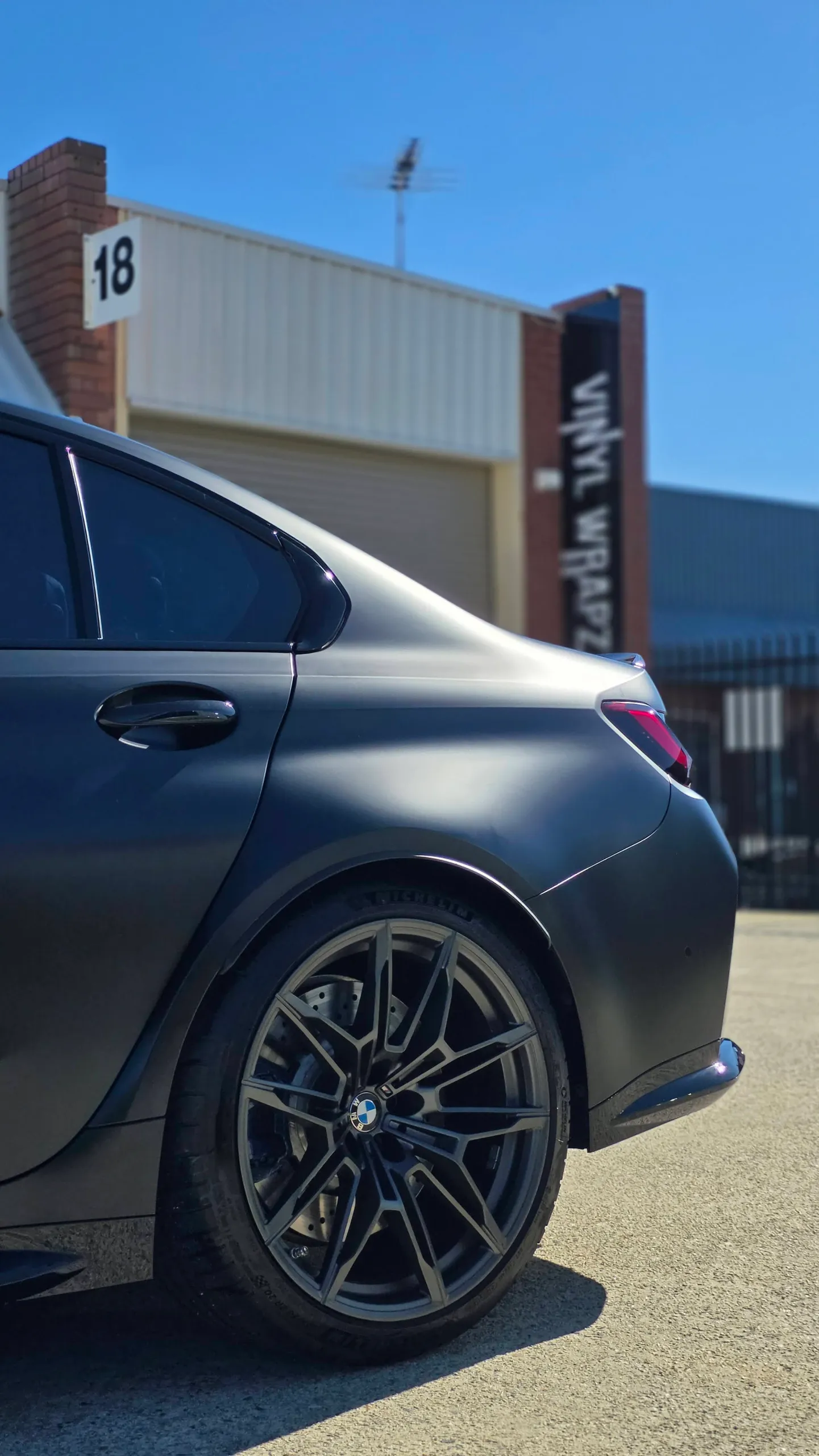 Satin grey BMW M3 Competition rear wheel and quarter panel in sunlight