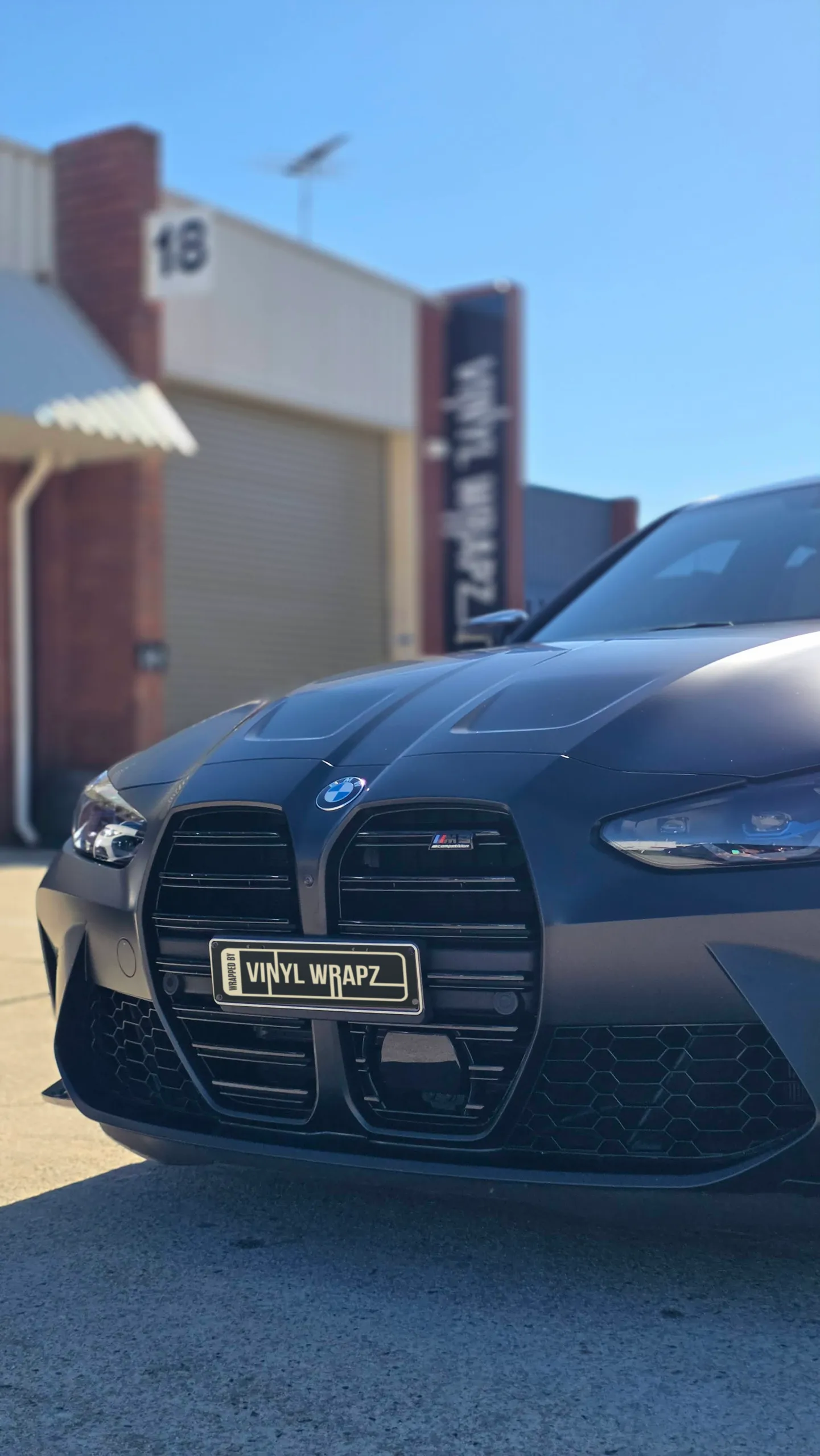 Front grille and headlight of a satin grey BMW M3 Competition outdoors