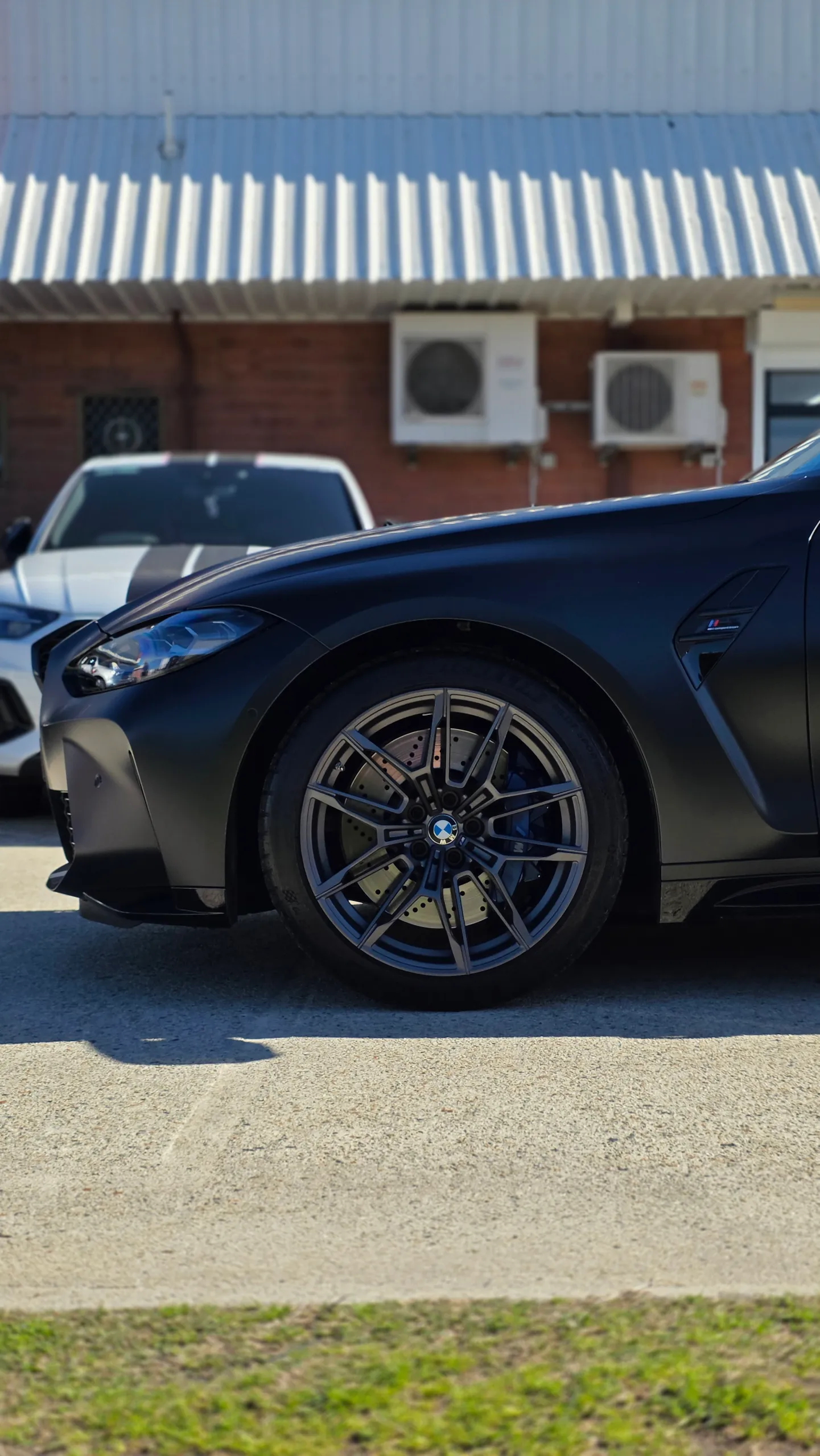 Satin grey BMW M3 Competition front wheel and guard, viewed from the side outdoors