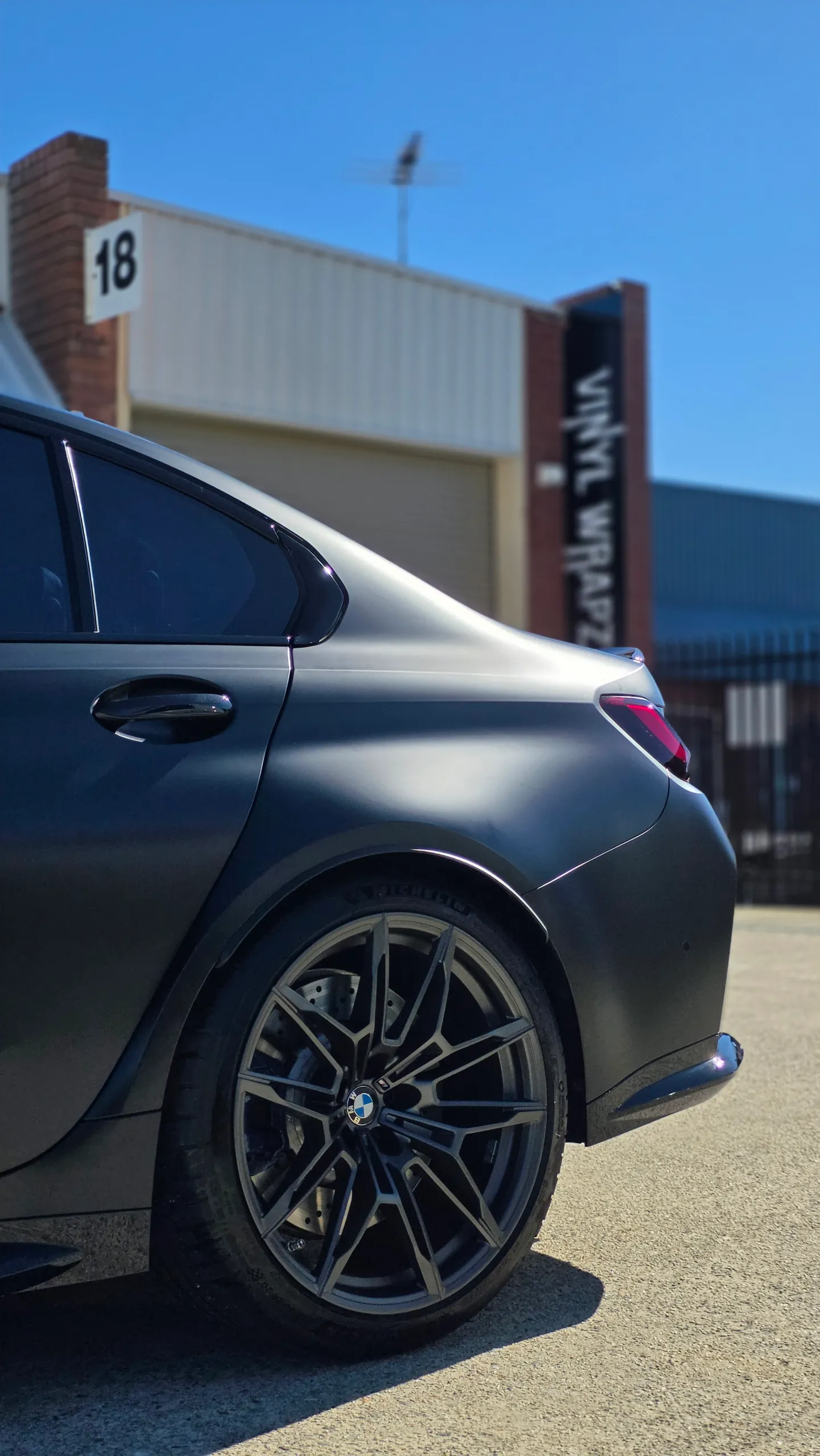 Satin grey BMW M3 Competition rear quarter and wheel outside the workshop