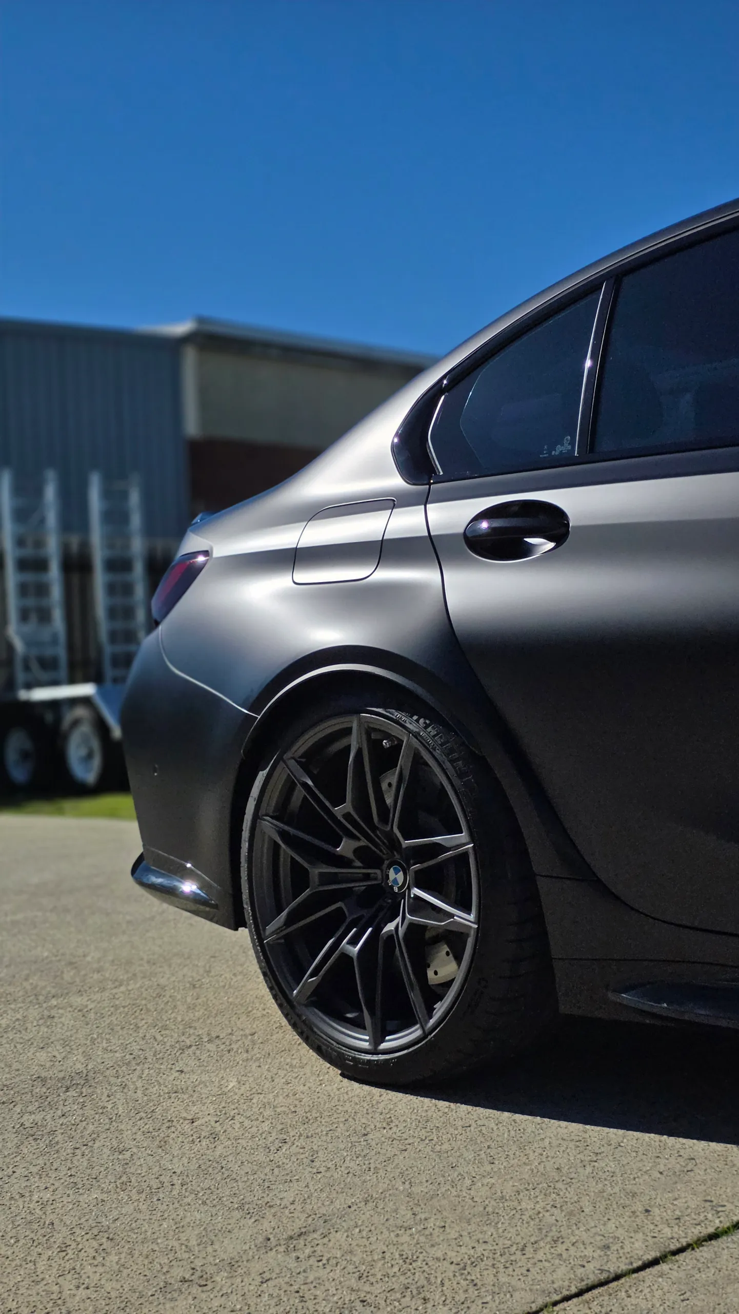 Satin grey BMW M3 Competition rear wheel and lower rear door in sunlight