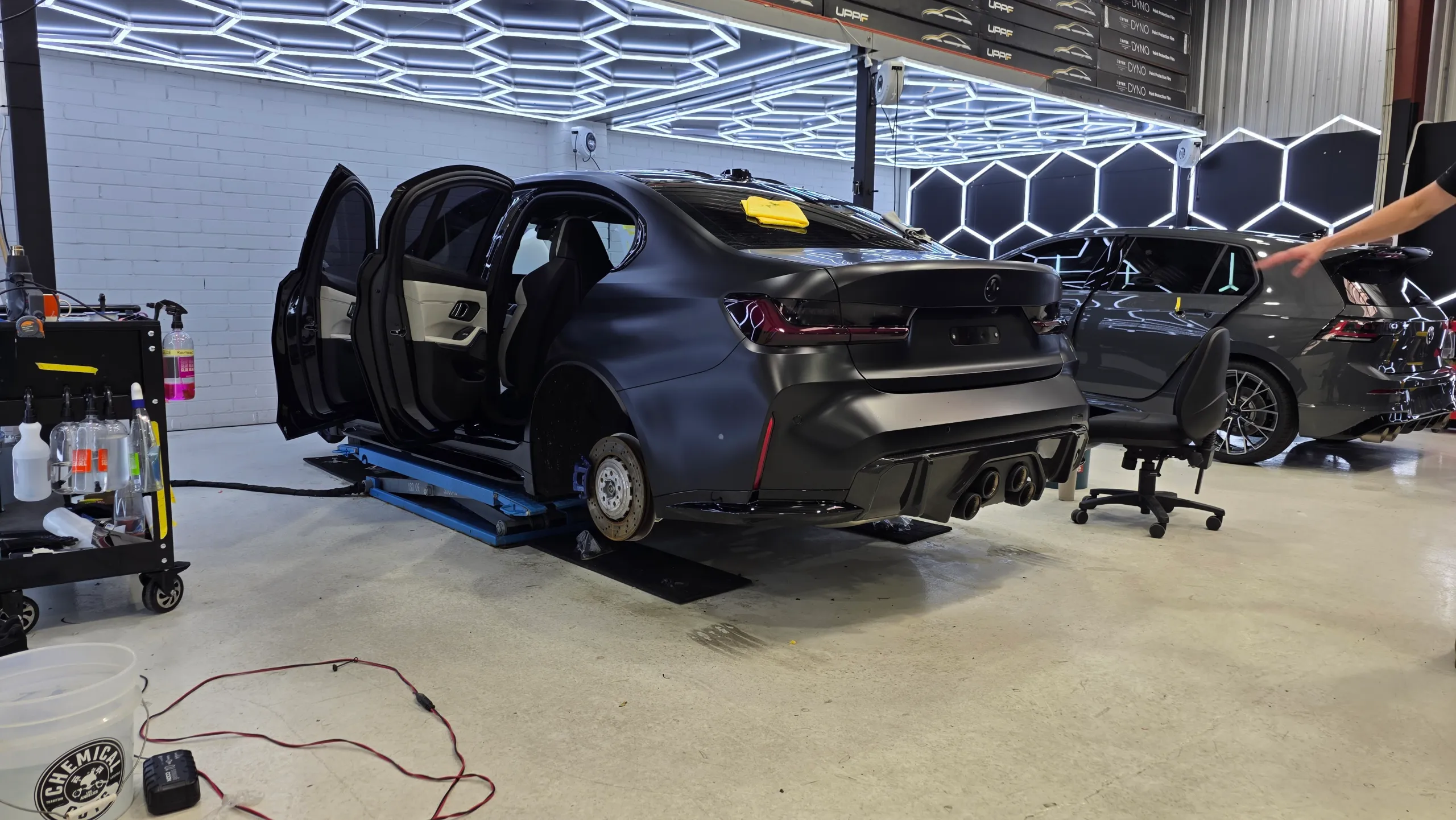 BMW M3 Competition on a workshop lift with doors open and a rear wheel removed