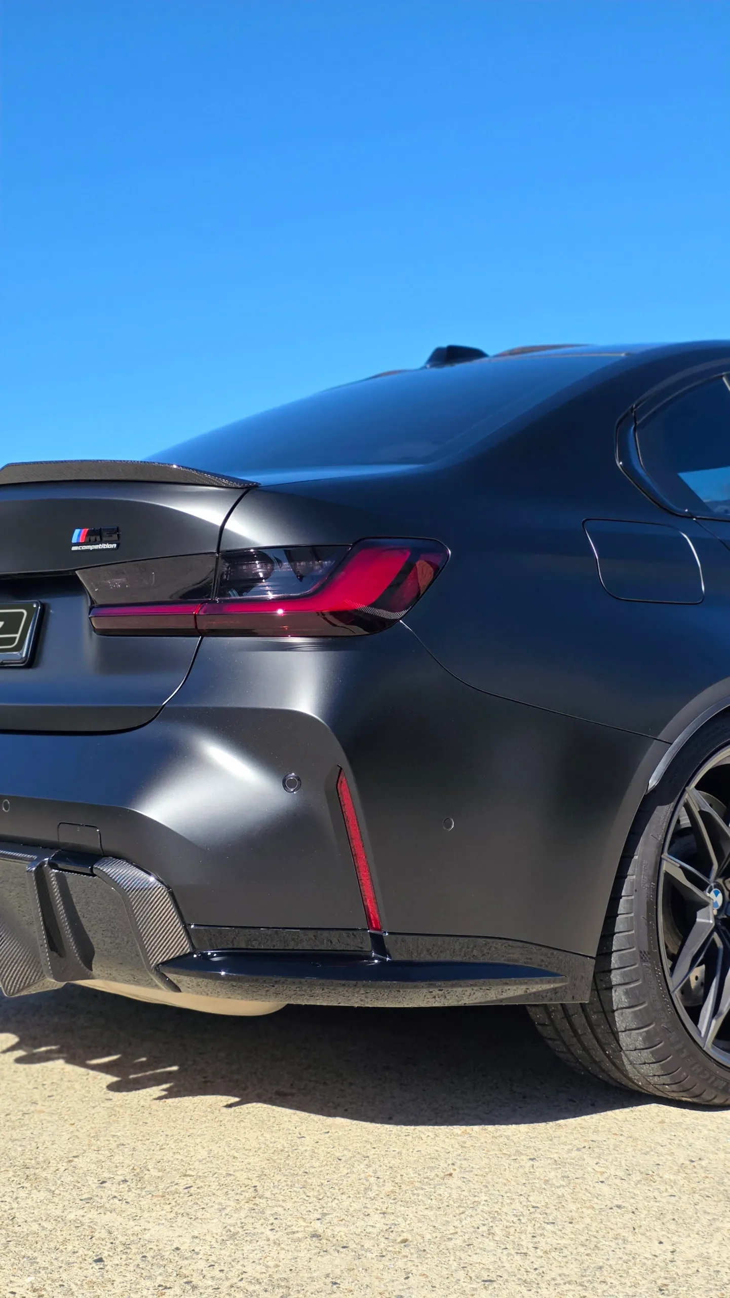 Rear bumper, tail light and satin grey quarter panel of a BMW M3 Competition outdoors