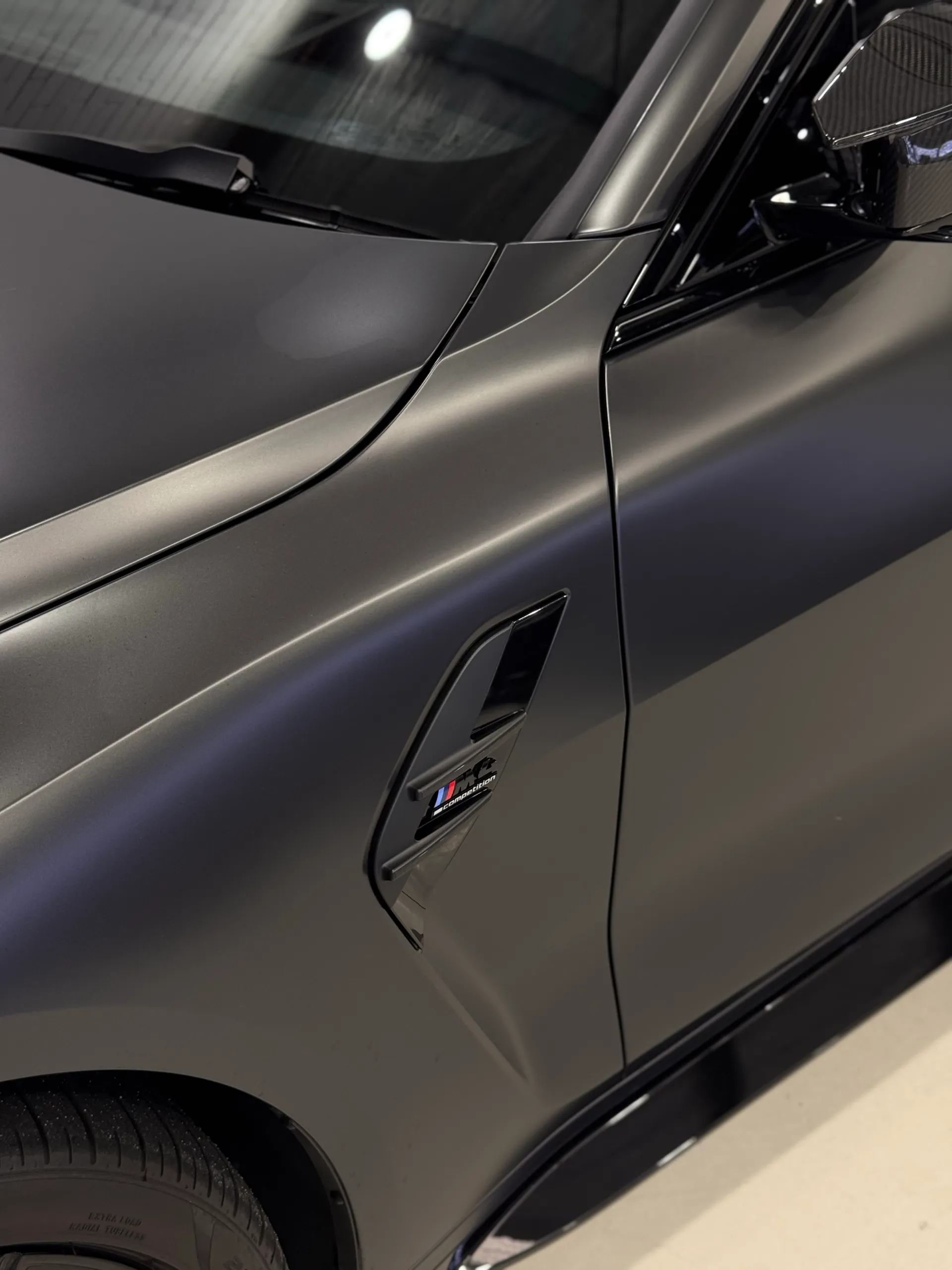 BMW M4 guard badge beside the satin dark grey front door and bonnet