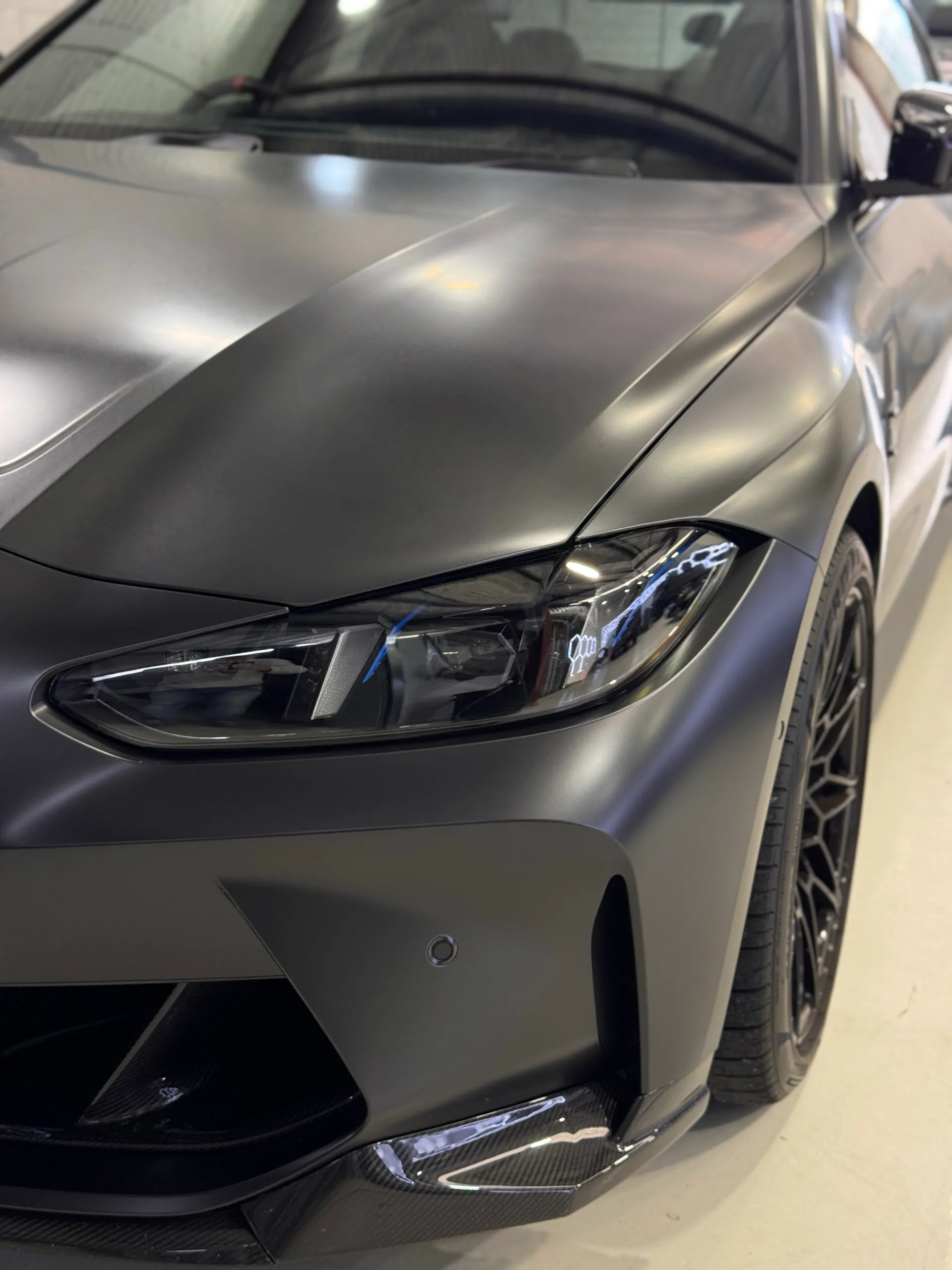 Satin dark grey BMW M4 Competition headlight and front bumper inside the workshop
