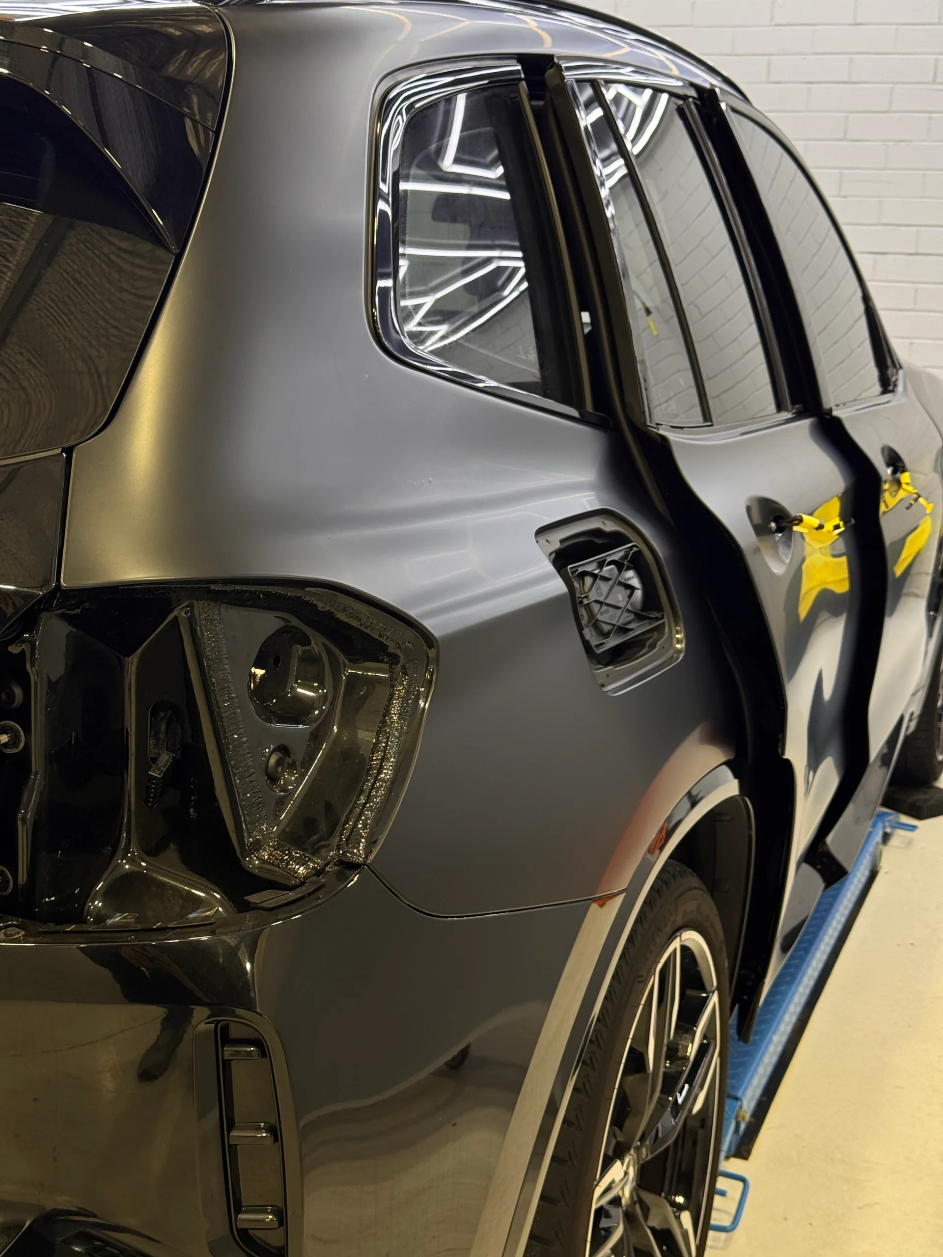 BMW X3 rear quarter during film installation, with its rear light and fuel filler flap removed