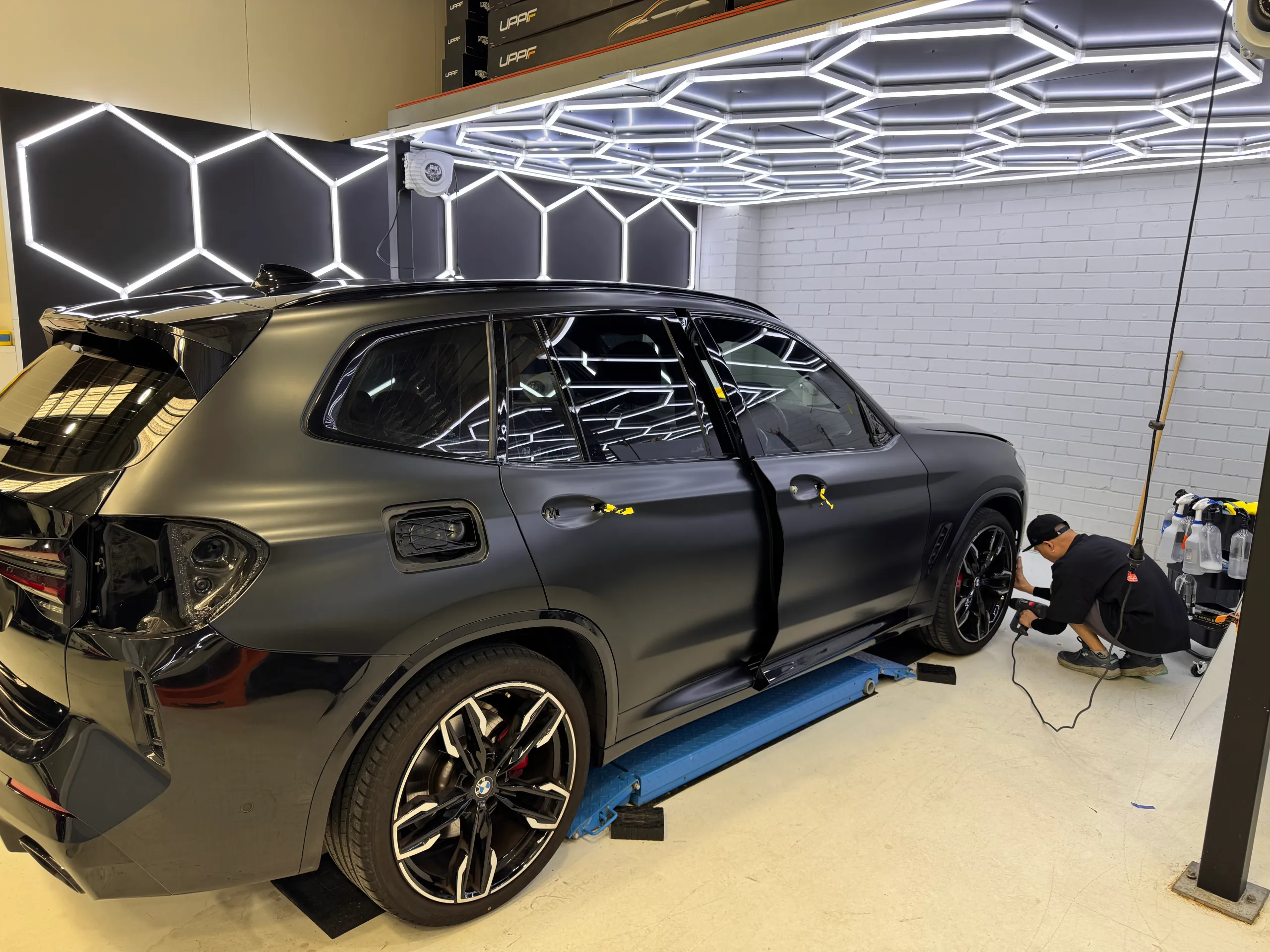 Installer working beside a dark grey BMW X3 on a lift with rear lights and door handles removed