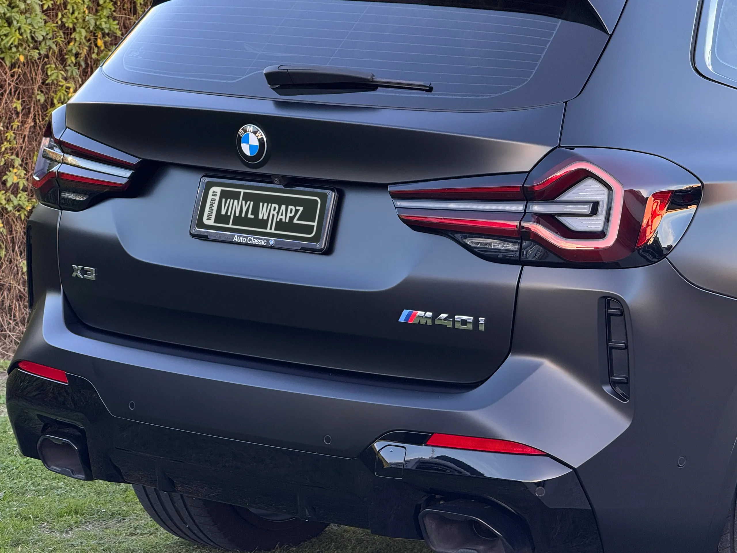 Matte dark grey BMW X3 M40i tailgate and rear lights outdoors, with both model badges visible
