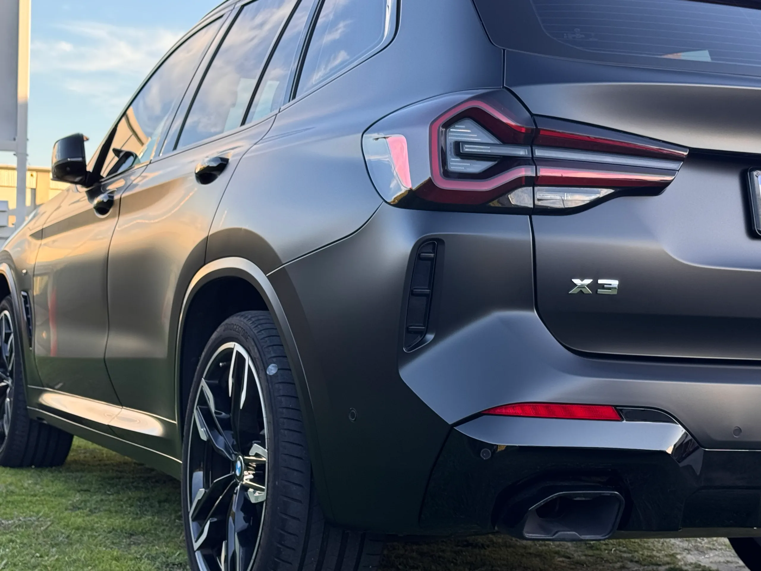 Matte dark grey BMW X3 M40i rear quarter, wheel and tail light outdoors