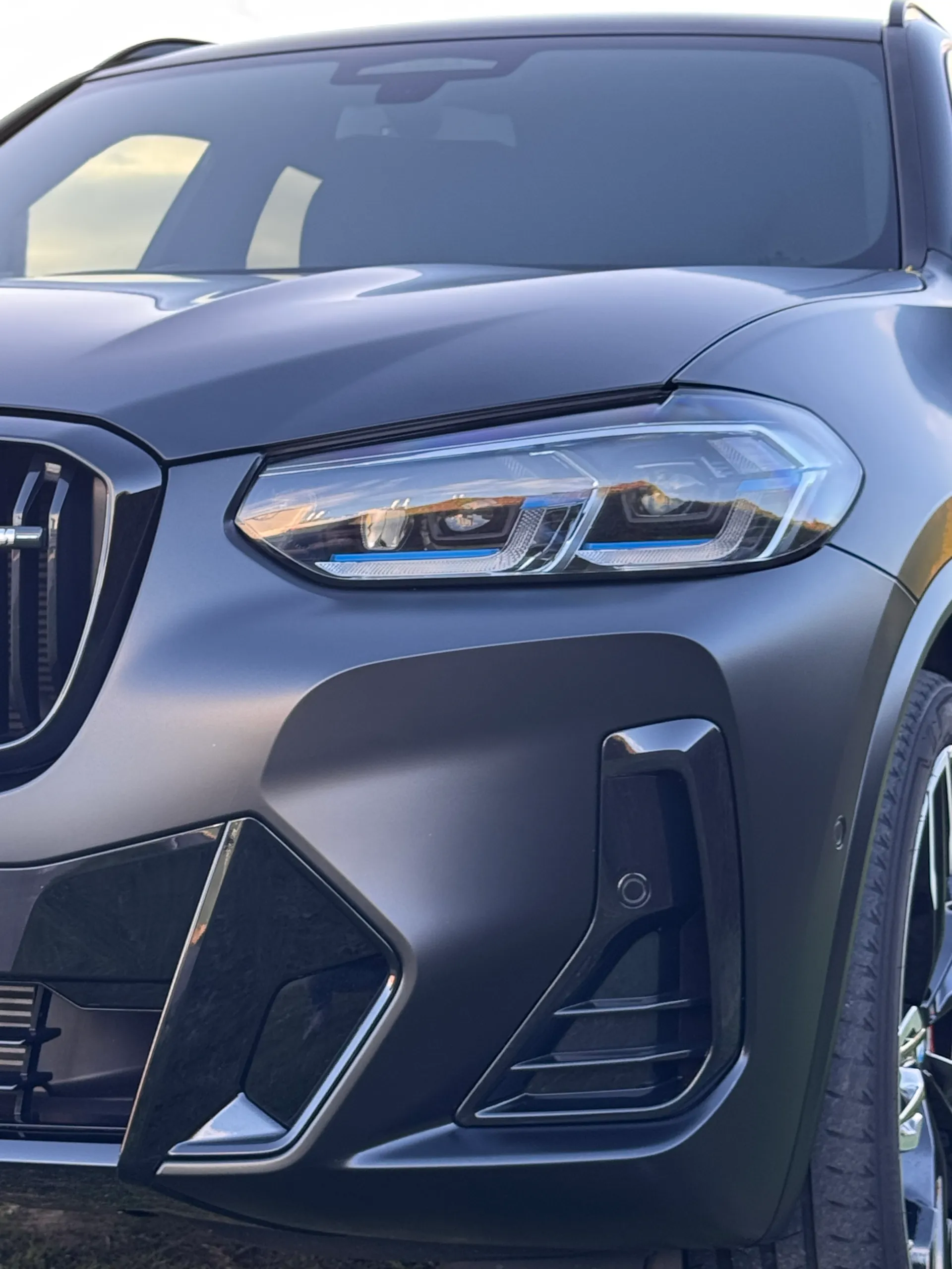Close-up of a matte dark grey BMW X3 M40i headlight and front bumper