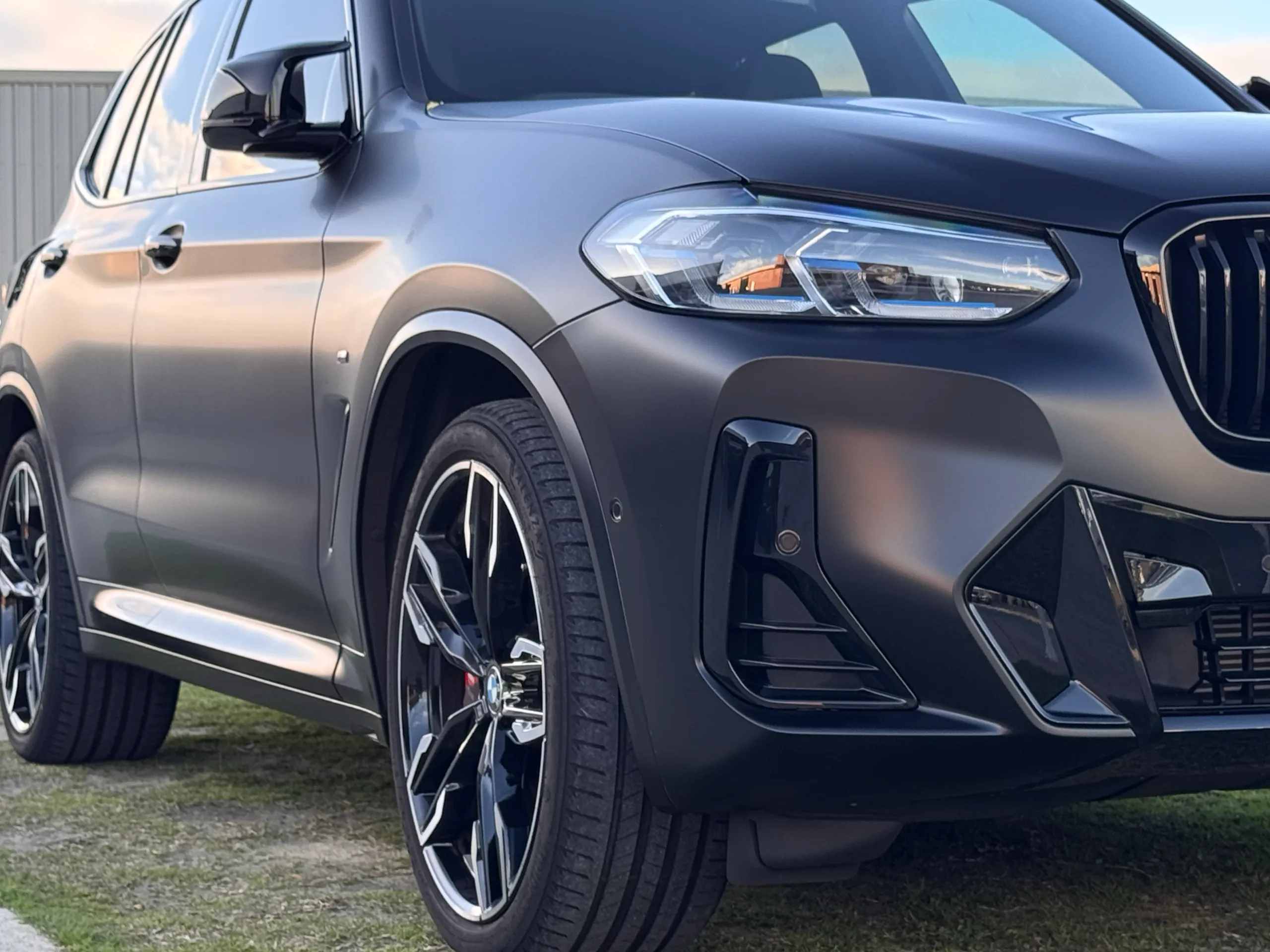 Matte dark grey BMW X3 M40i front quarter and side parked on grass