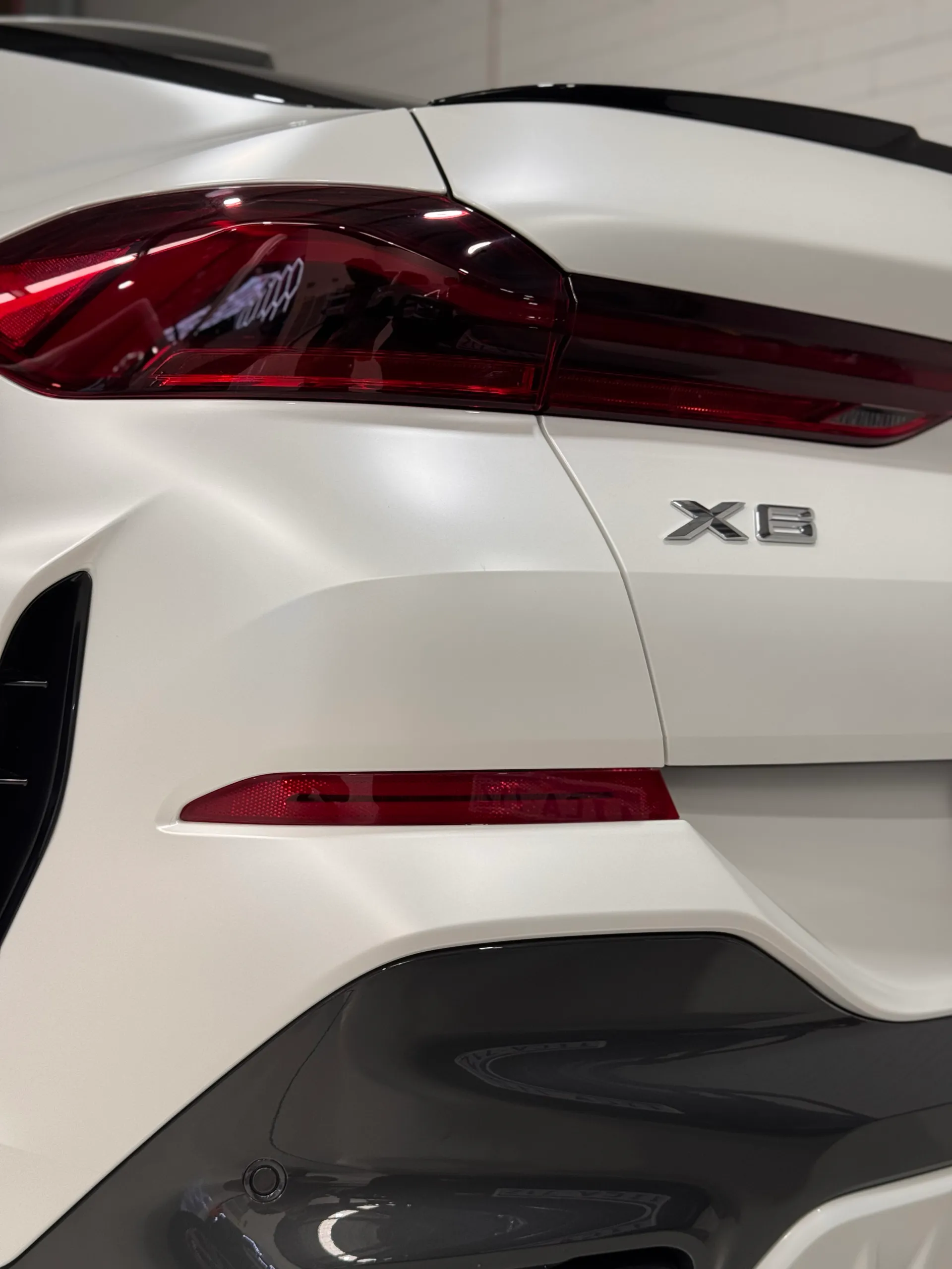 BMW X6 badge and red rear light against satin white tailgate bodywork