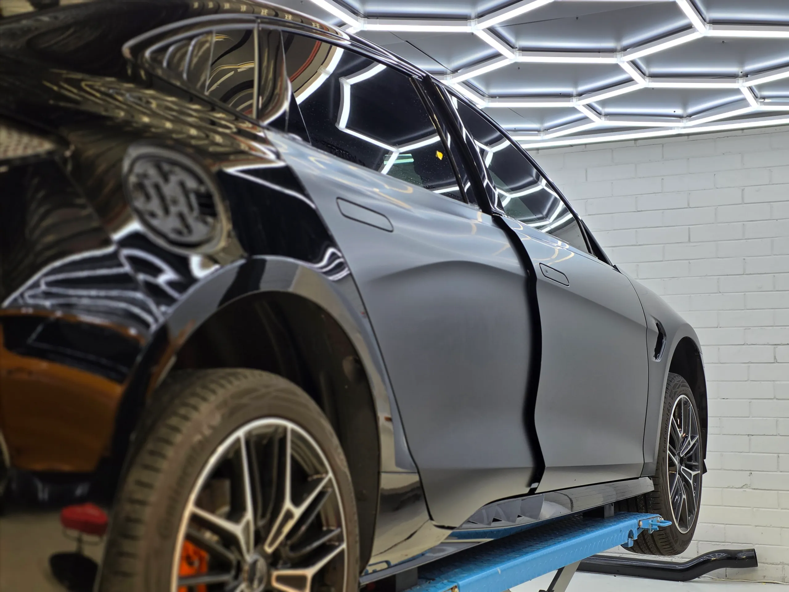 Satin film on the BYD Seal doors beside gloss black panels during installation on a workshop lift
