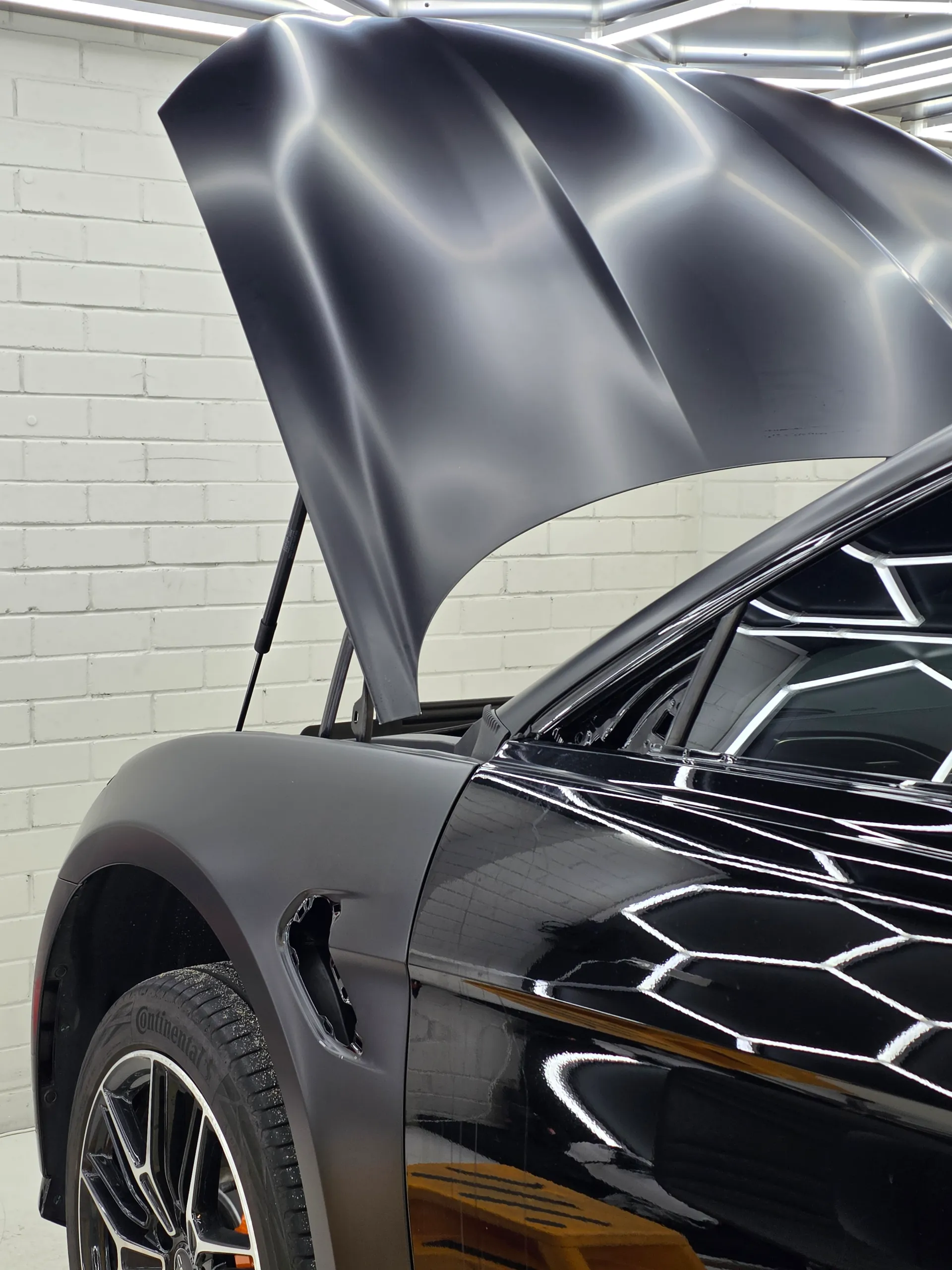 Raised satin black BYD Seal bonnet beside a gloss door during film installation