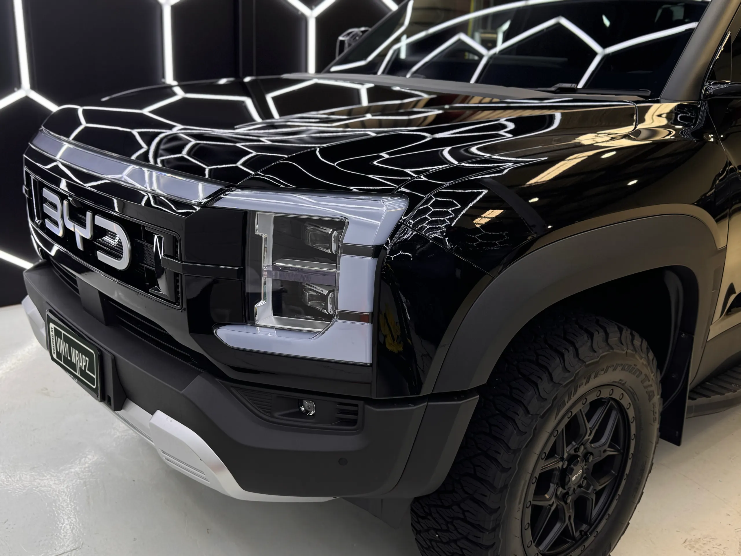 BYD grille, headlight and gloss black bonnet reflecting hexagonal workshop lighting