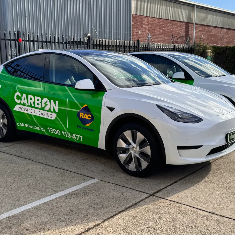 Two white Tesla Model Y vehicles with green Carbon novated leasing graphics