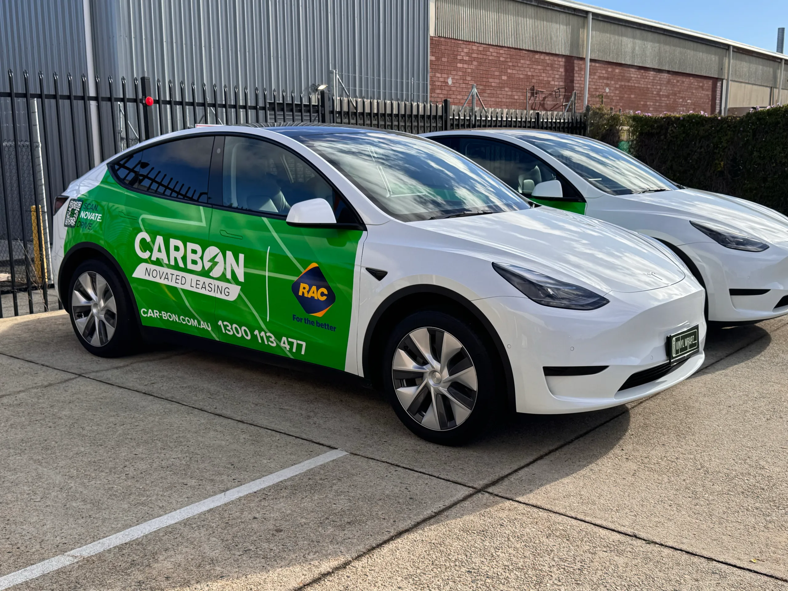 Two white Tesla Model Y vehicles with green Carbon novated leasing graphics