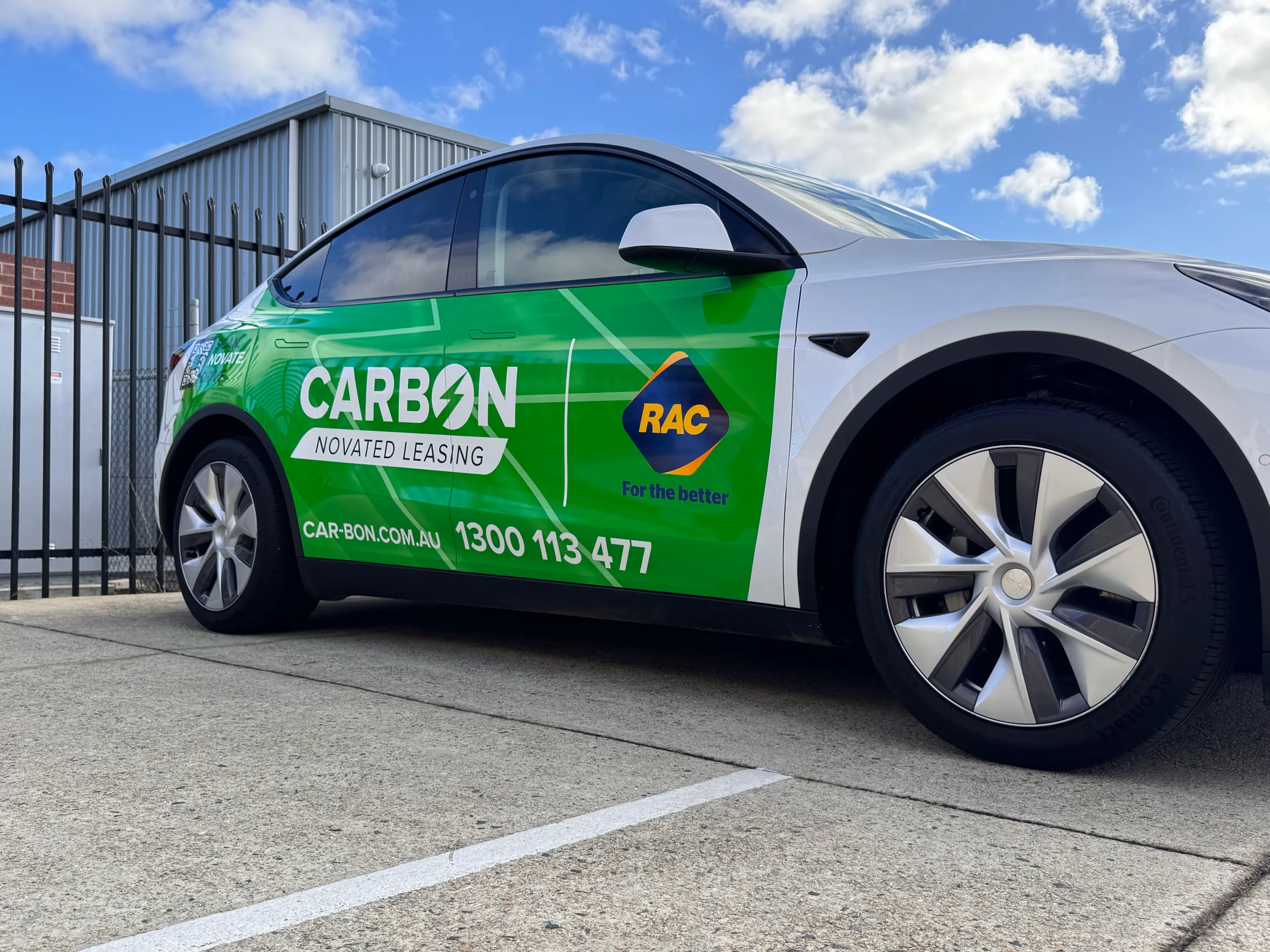 Low front-quarter view of a white Tesla Model Y with green Carbon graphics