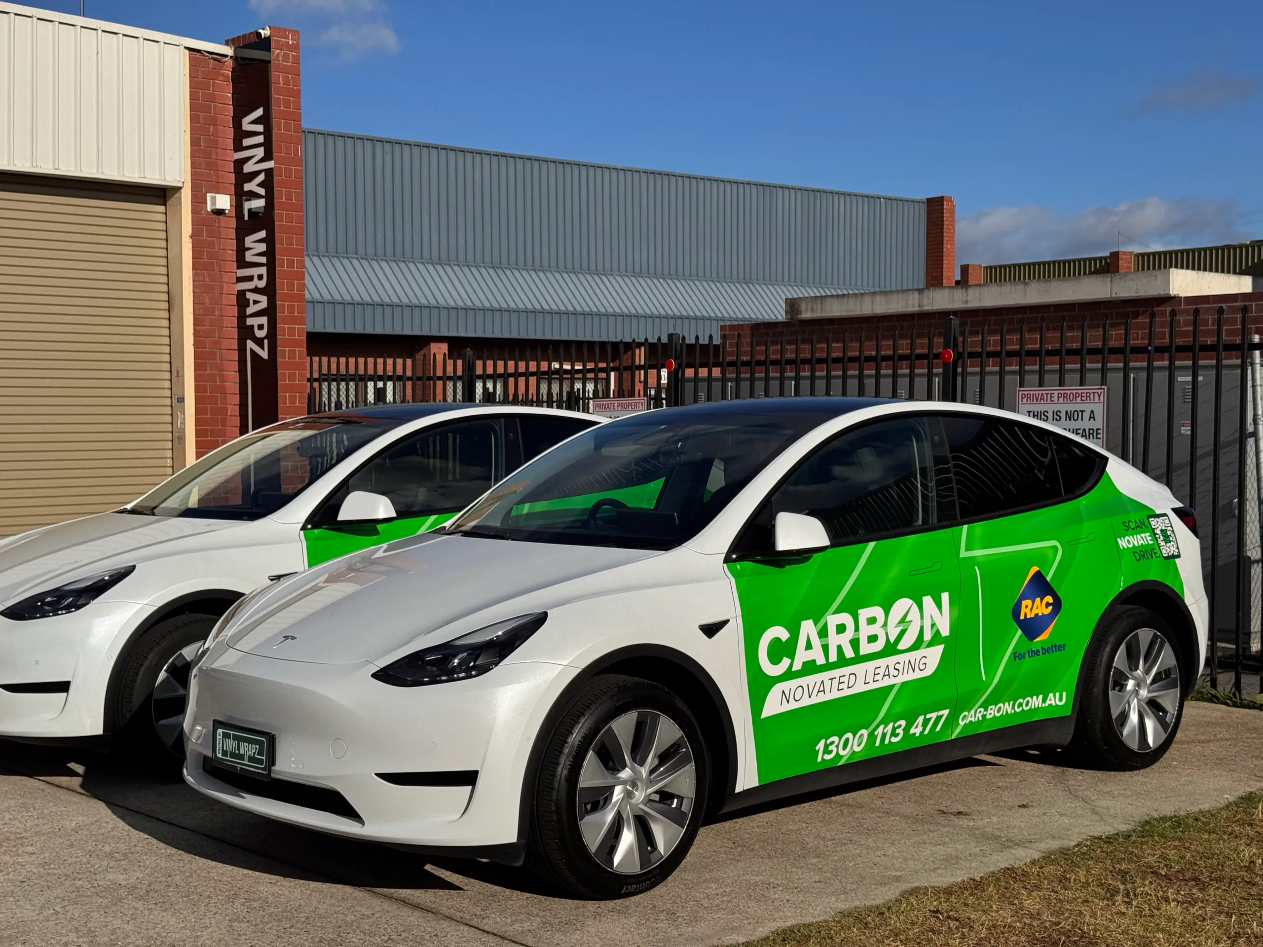 Carbon and RAC graphics on two white Tesla Model Y vehicles outdoors