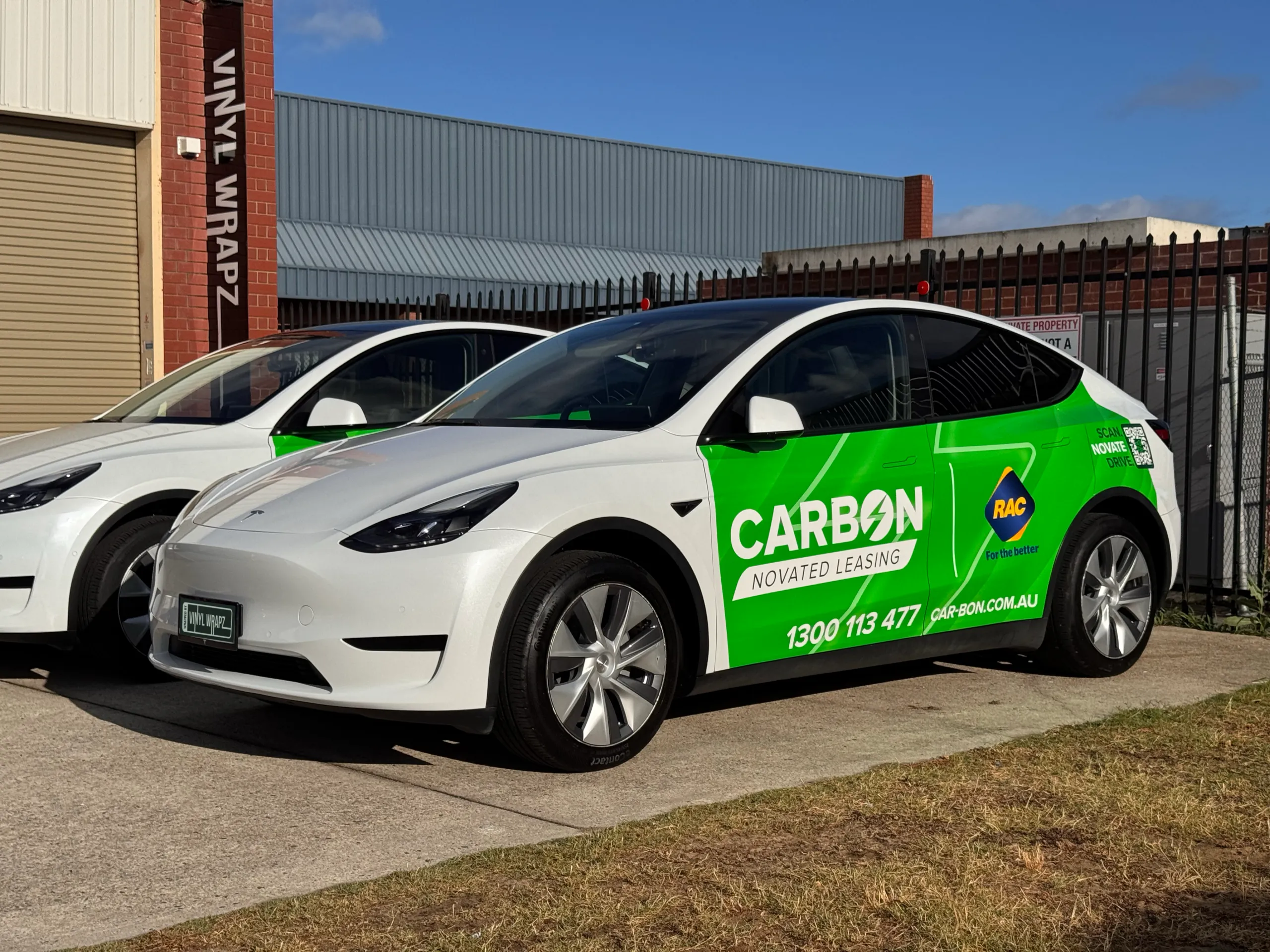 White Tesla Model Y with green Carbon graphics and a second branded Tesla behind it