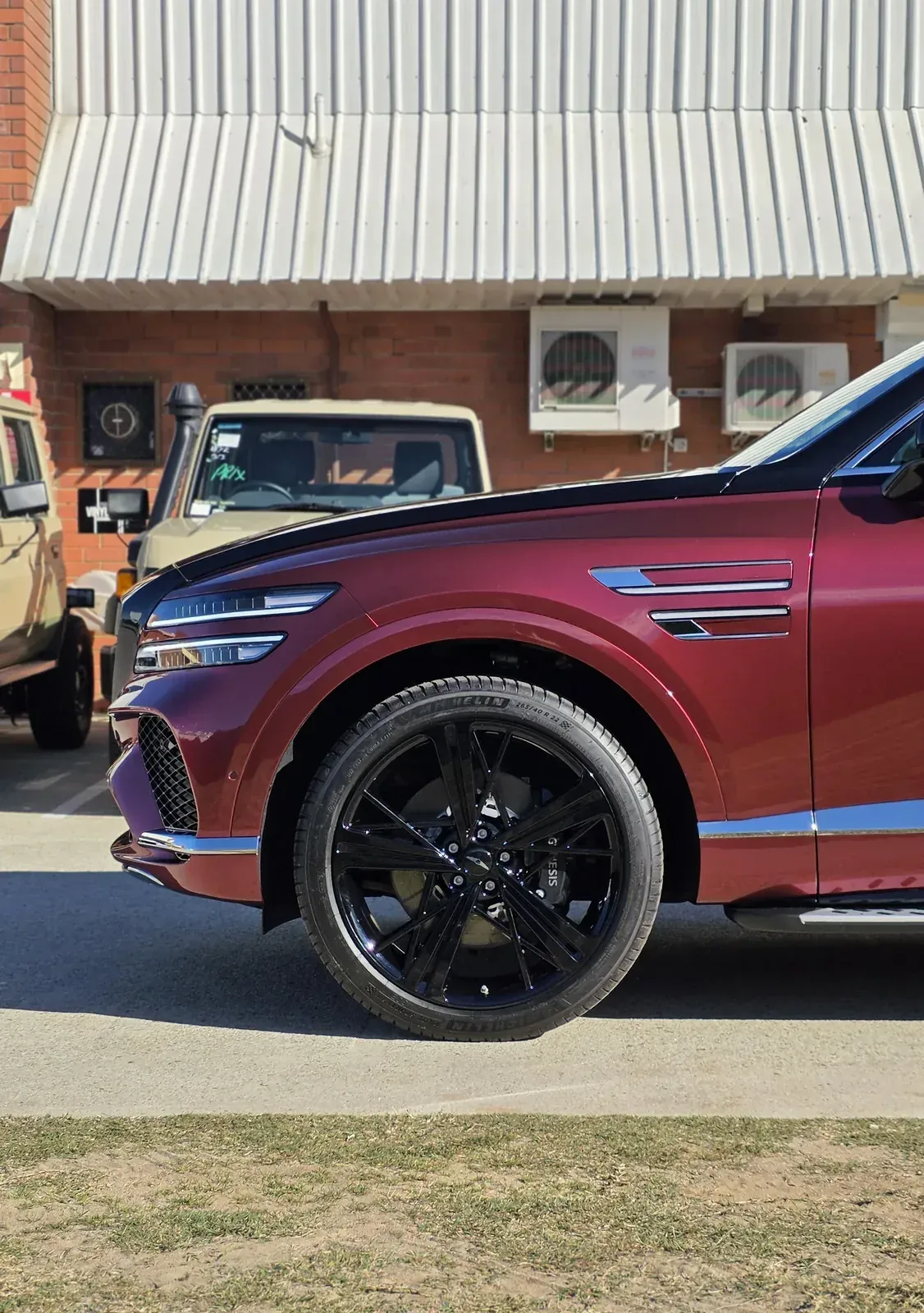 Genesis GV80 Coupe in a two-tone red wrap, front quarter and wheel outside the workshop