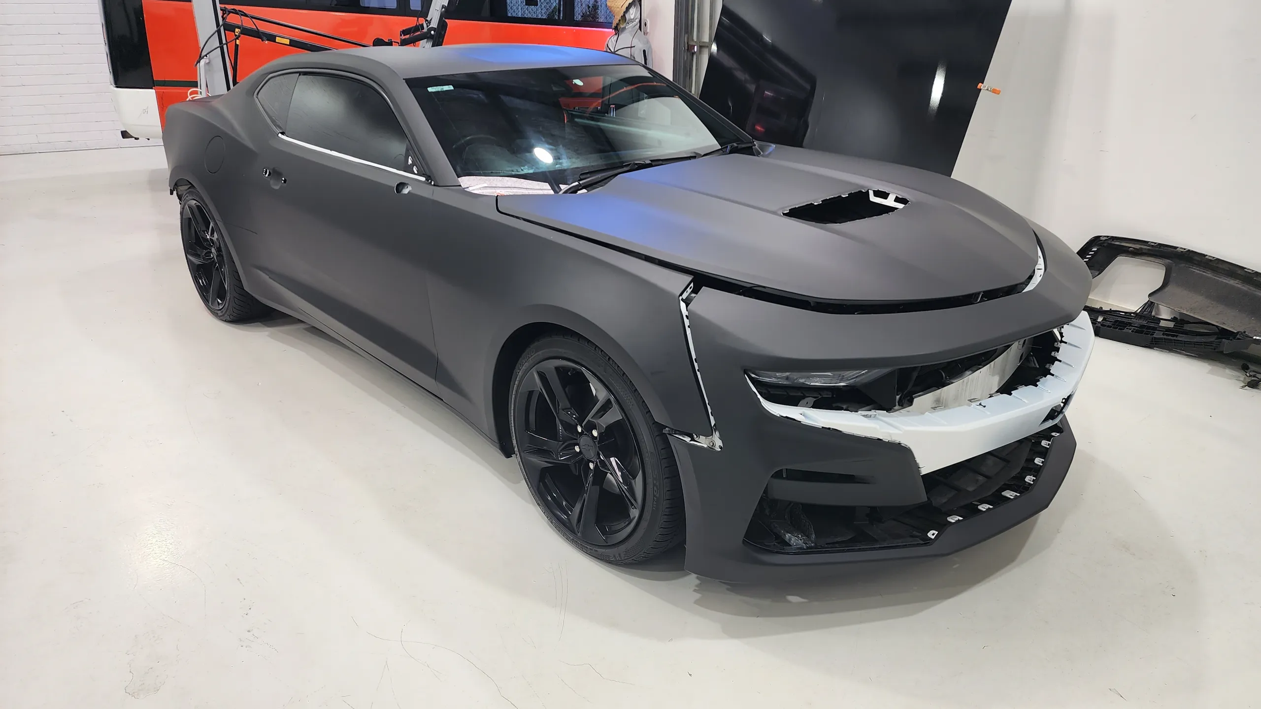 Matte black Chevrolet Camaro SS during colour-change installation, with its doors closed and front trim removed