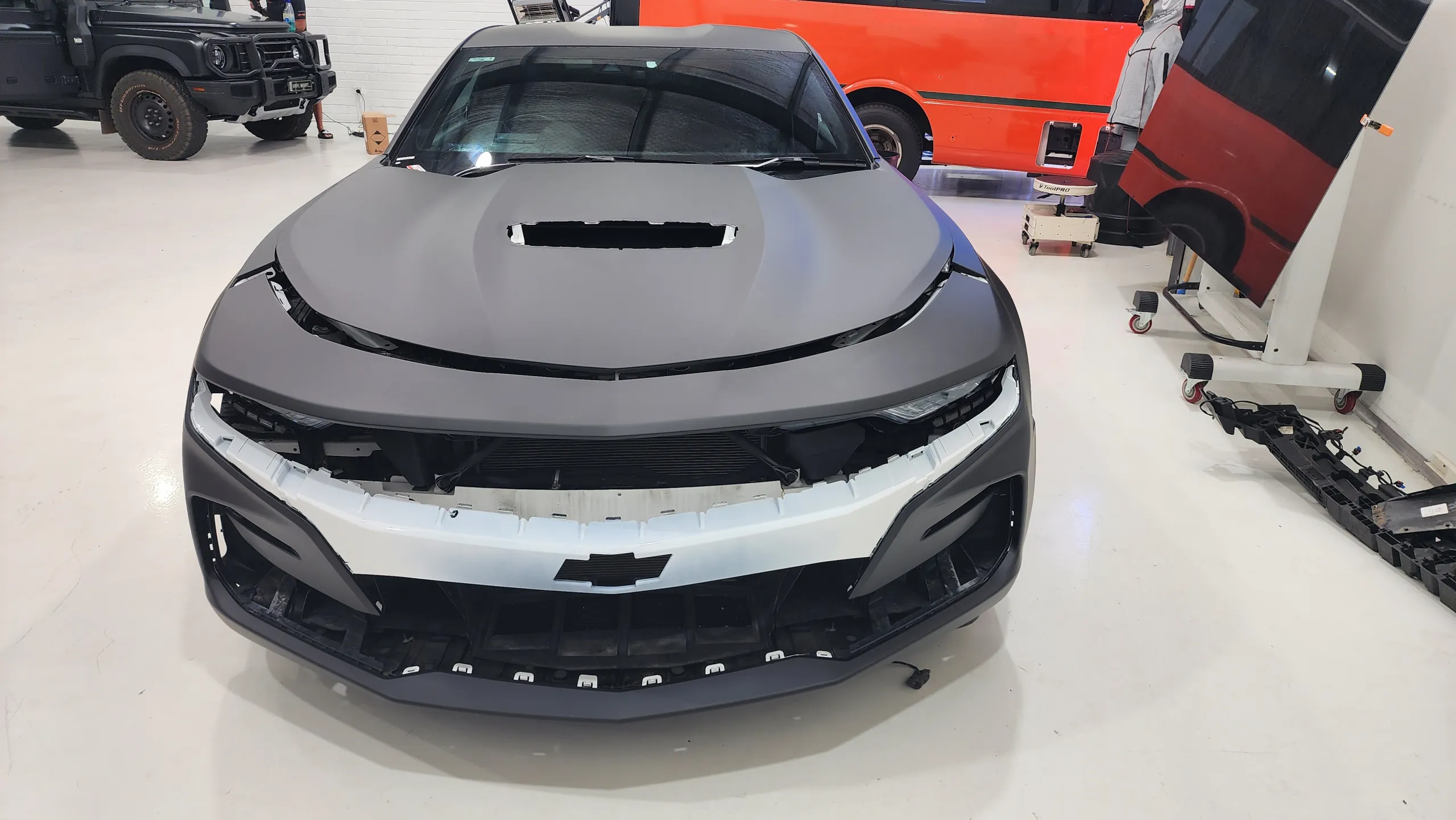 Front view of the Camaro during wrapping, with white bumper sections still exposed