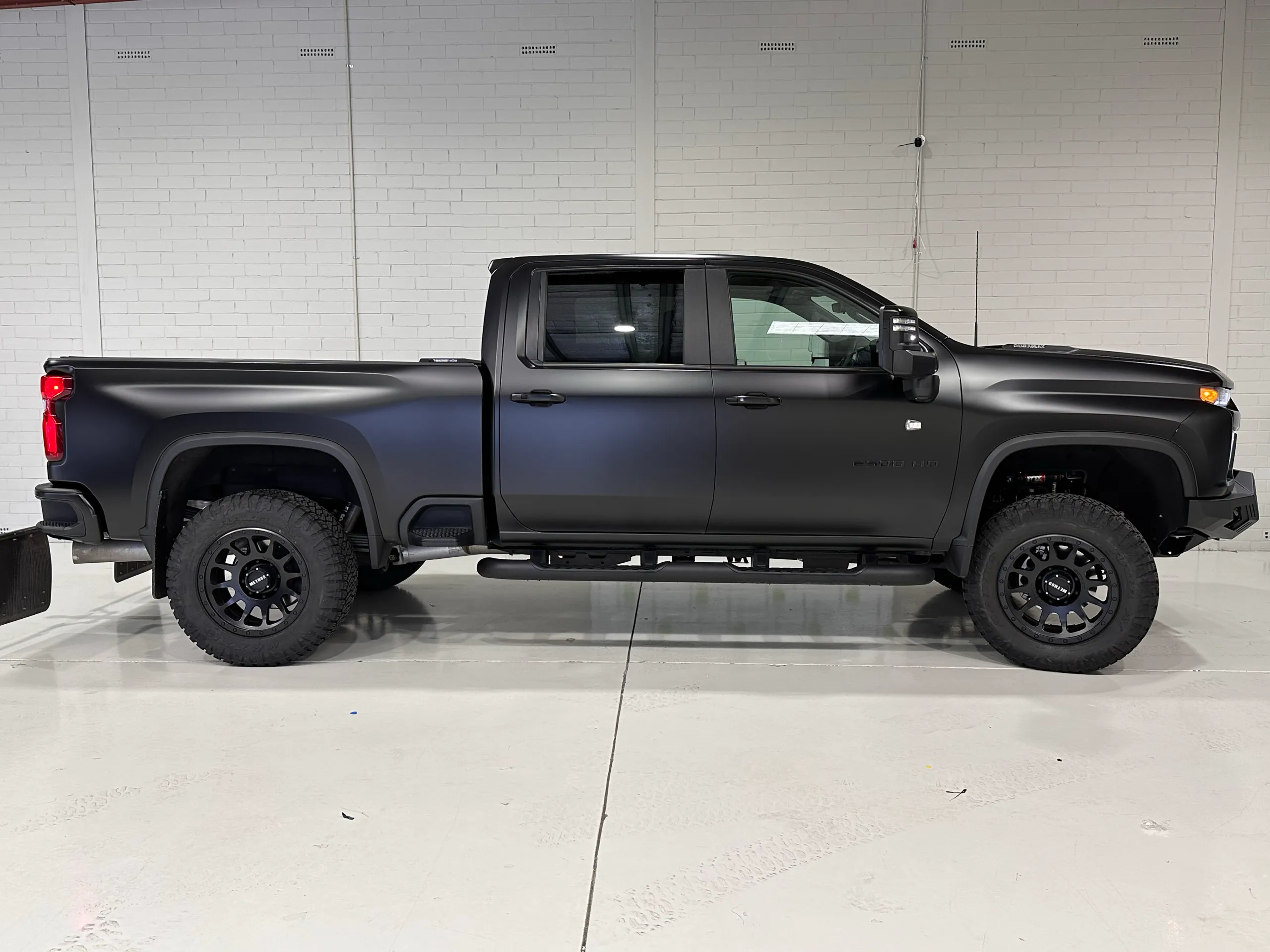 Matte black Chevrolet Silverado 2500 HD in side profile against a white workshop wall
