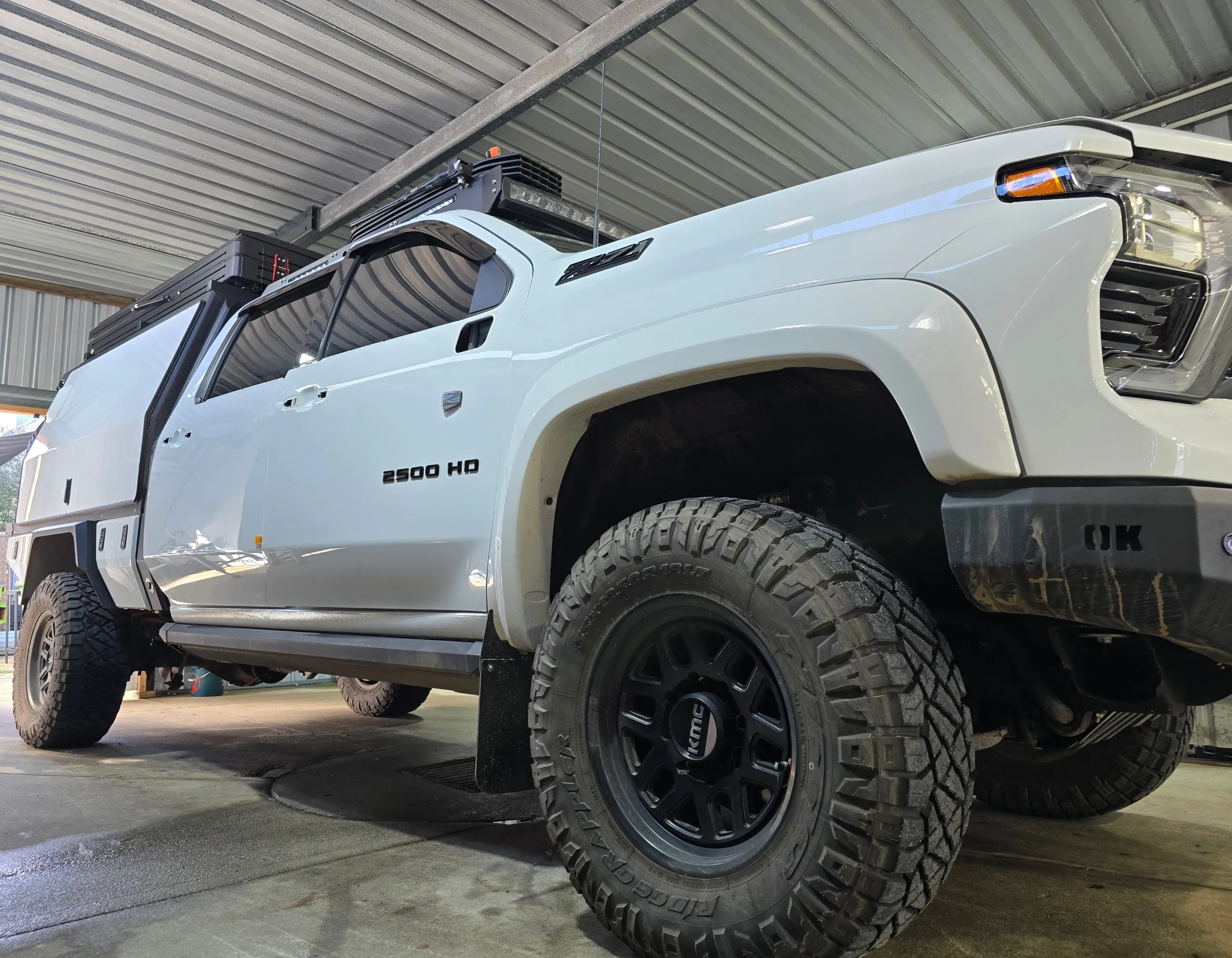 Low view of a white Chevrolet Silverado 2500 HD with a canopy inside the workshop