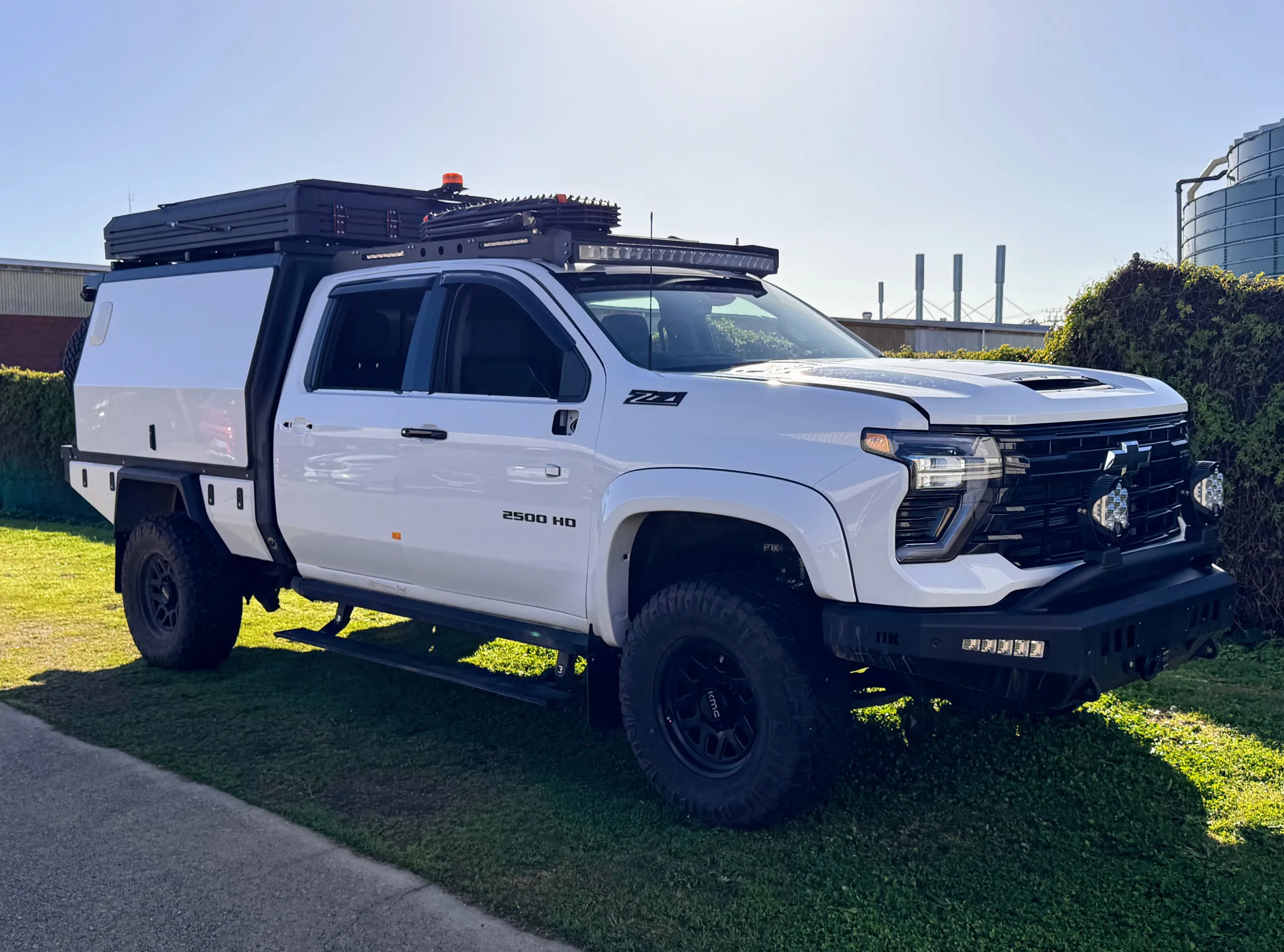 White Chevrolet Silverado 2500 HD with a canopy and roof equipment parked on grass