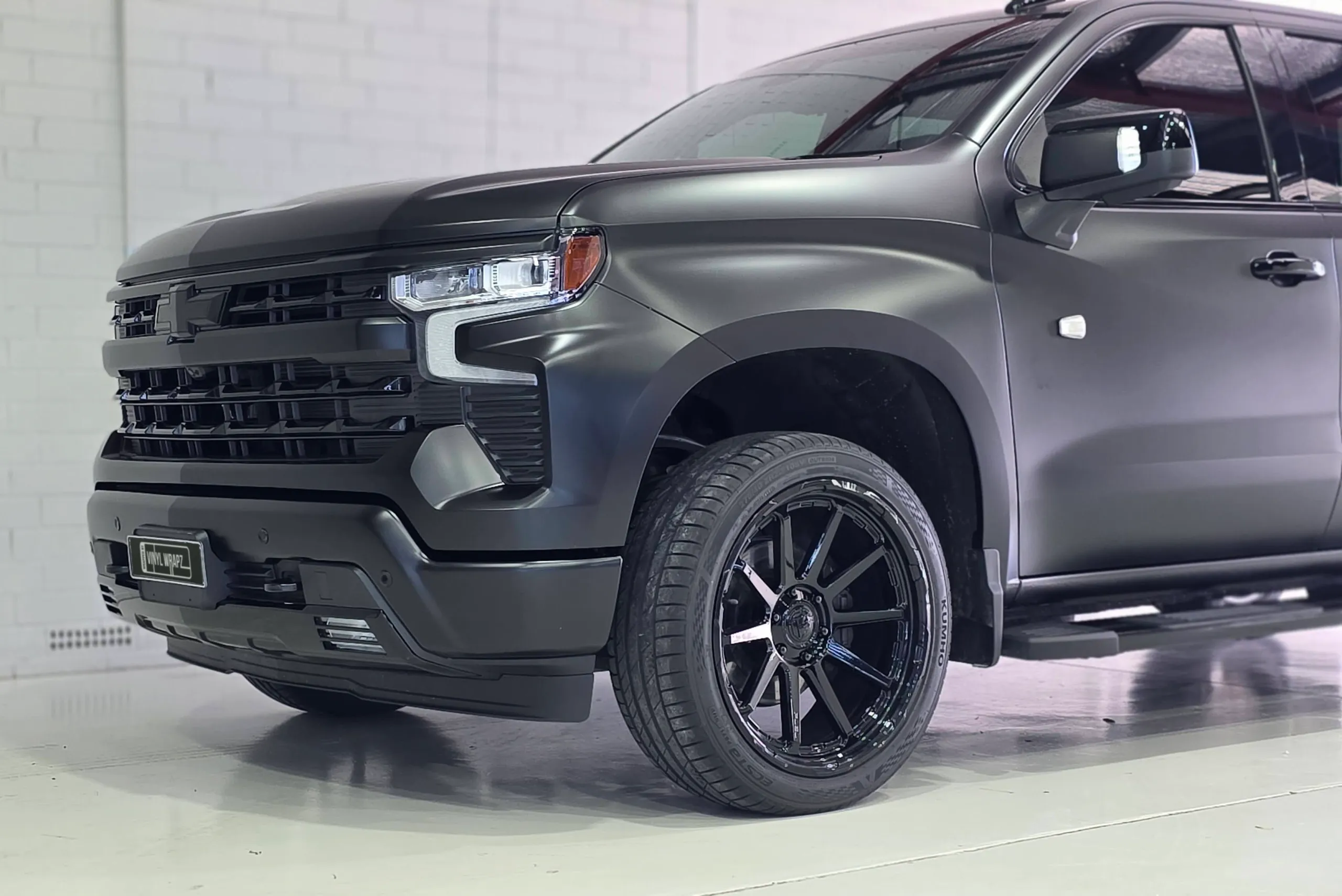 Satin black Silverado grille, headlight and front wheel against a white workshop wall