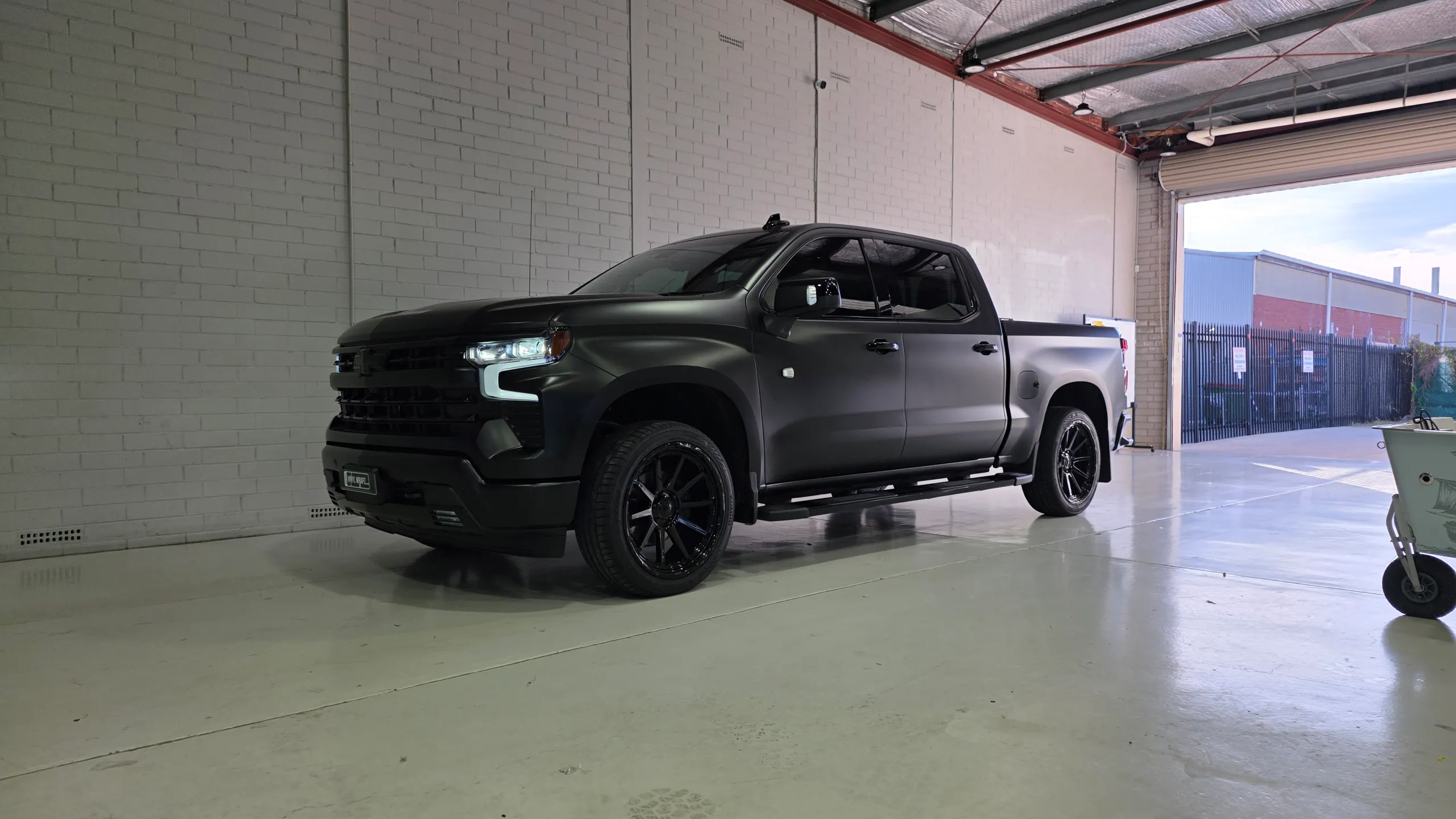 Wide workshop view of the satin black Chevrolet Silverado with black wheels