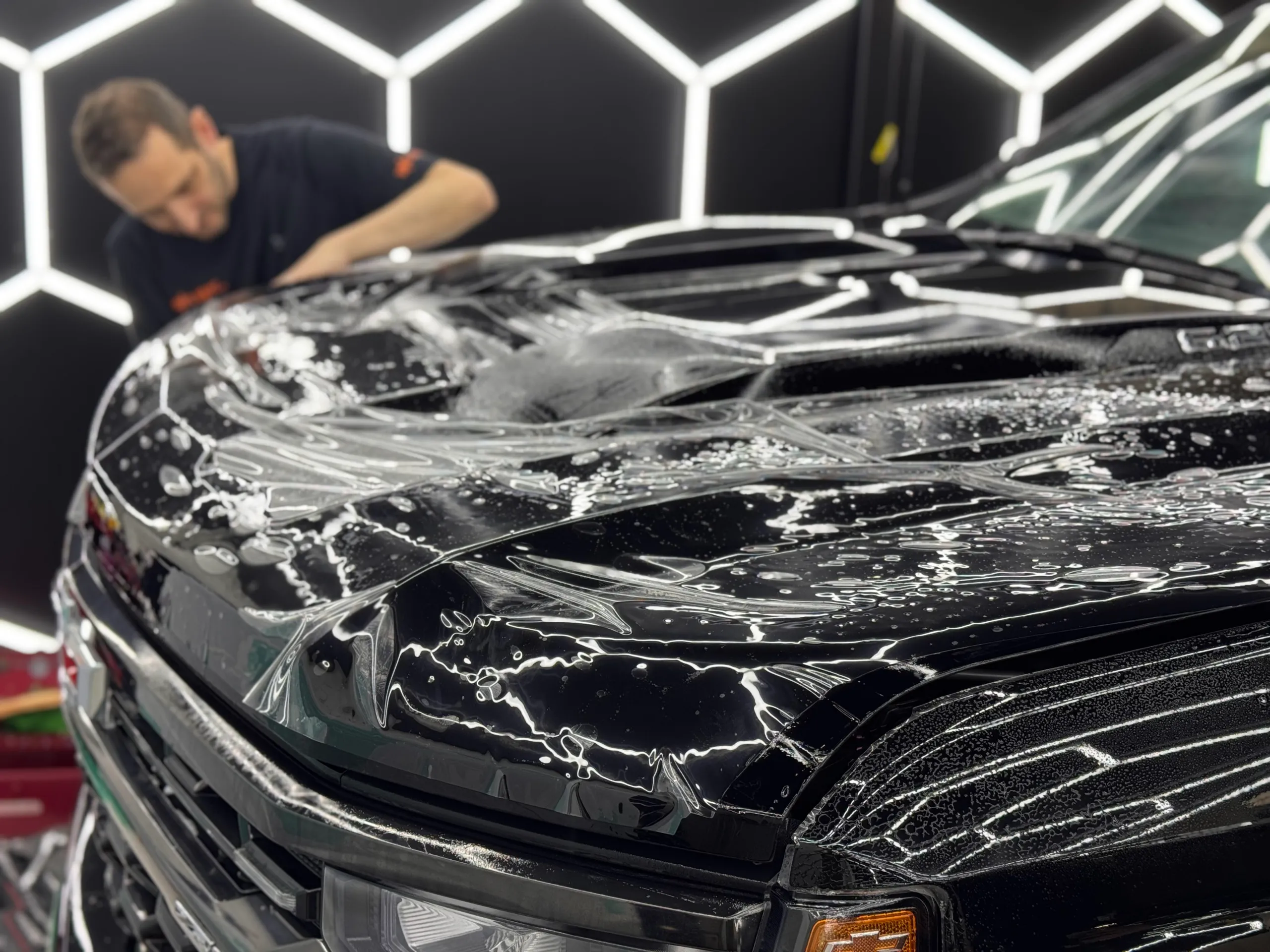 Installer applying wet protective film across the black Chevrolet Silverado bonnet