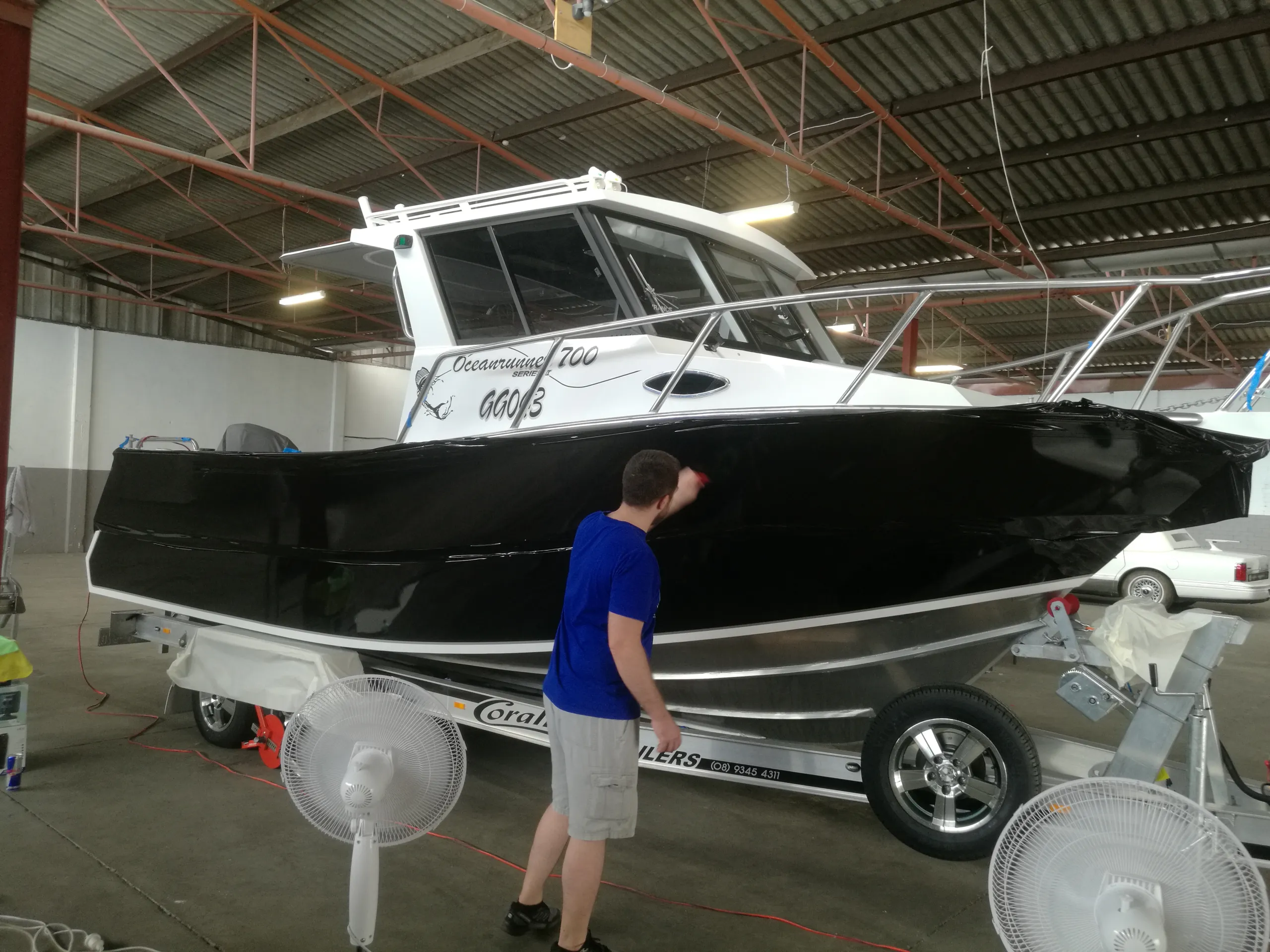 Installer working on the glossy black hull of a white-cabin Coraline fishing boat on its trailer