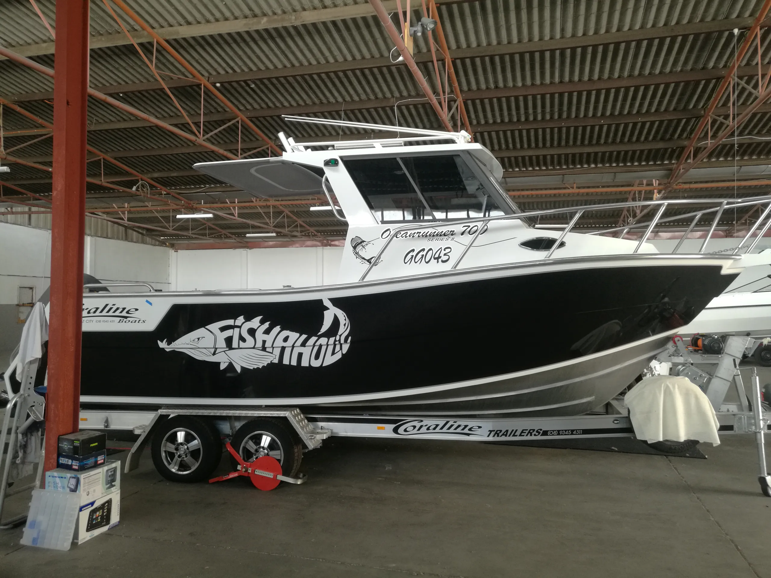 White-cabin Coraline boat with Fishaholic lettering on its glossy black hull inside a shed