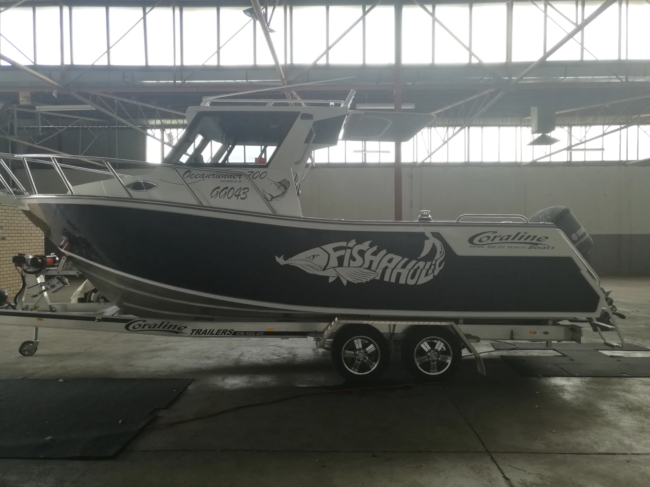 Backlit side view of the Fishaholic Coraline fishing boat on its trailer inside a shed