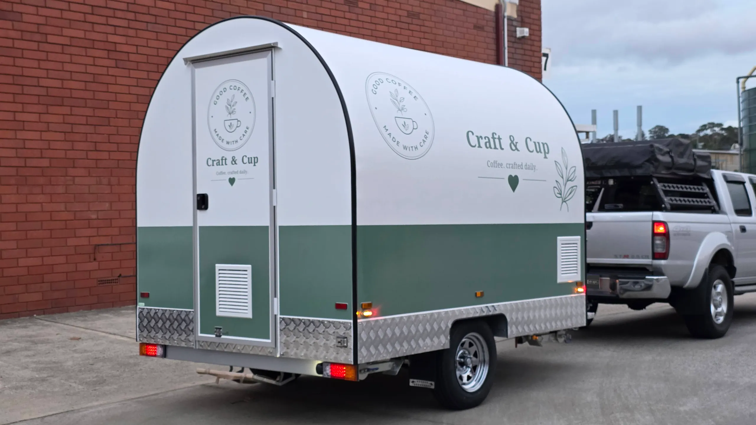 White and sage green Craft & Cup coffee trailer with branding on its side and rear door