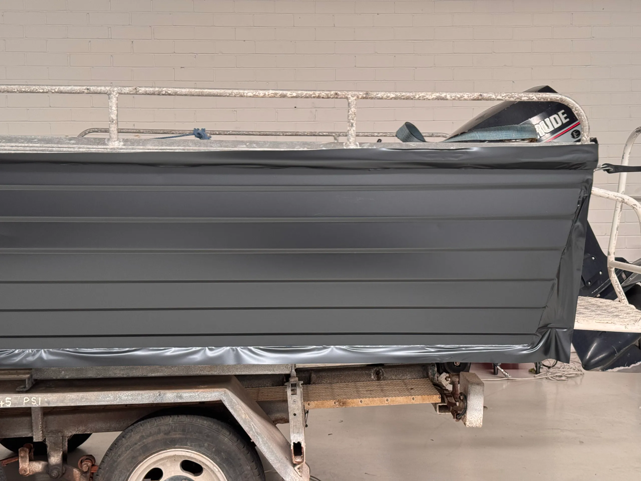 Dark grey film being fitted over the ridged side of an aluminium dinghy, with loose edges awaiting trimming
