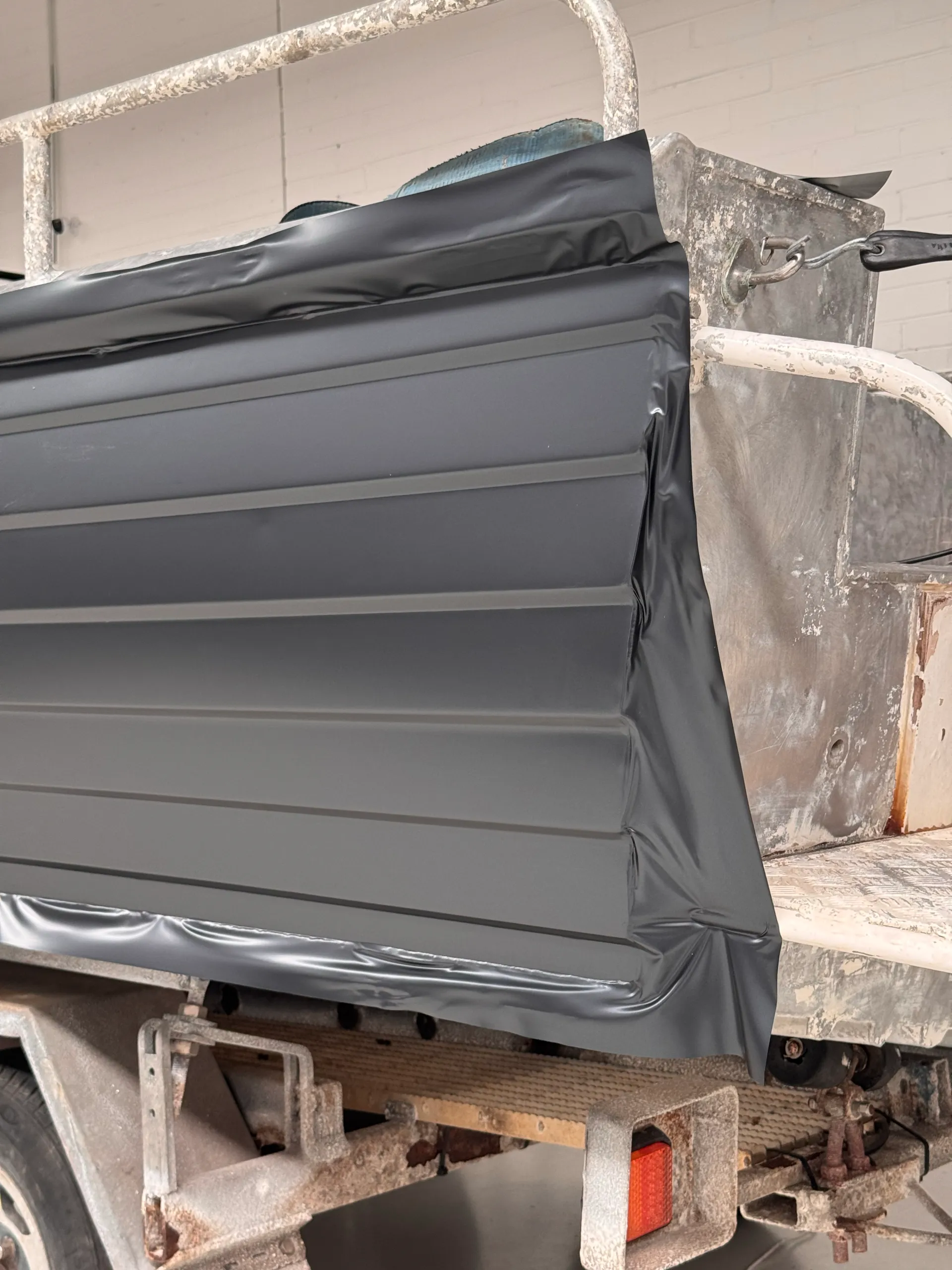 Grey wrap film around the stern corner of an aluminium dinghy, beside the bare aluminium transom