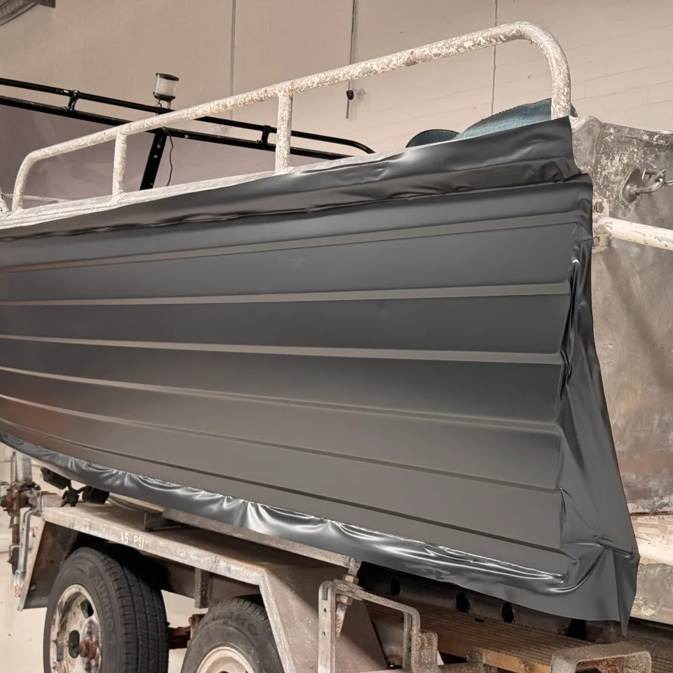 Aluminium dinghy on its trailer with grey film fitted along one side and excess film around the edges