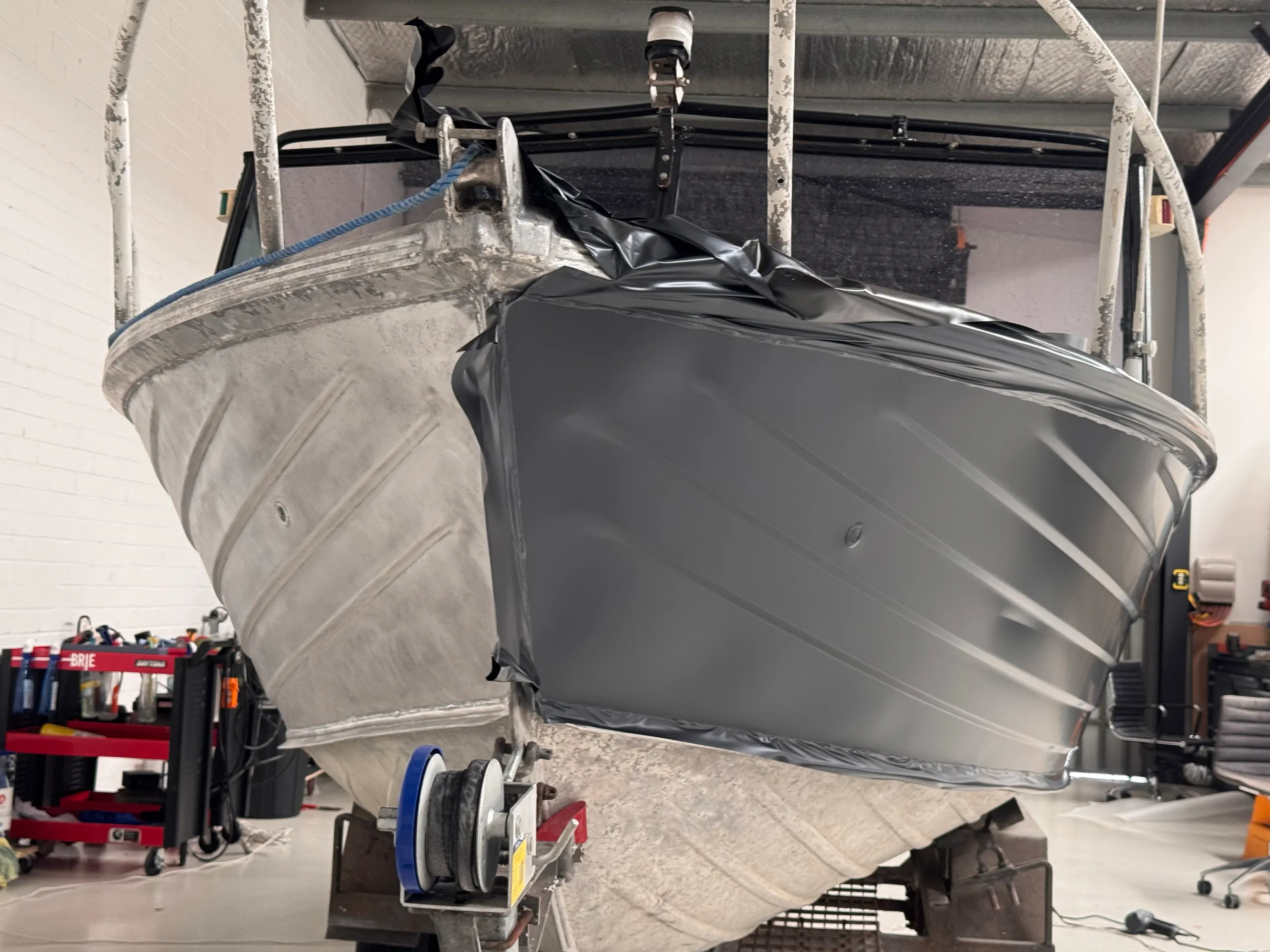 Bow of an aluminium dinghy showing bare metal on one side and grey wrap film on the other