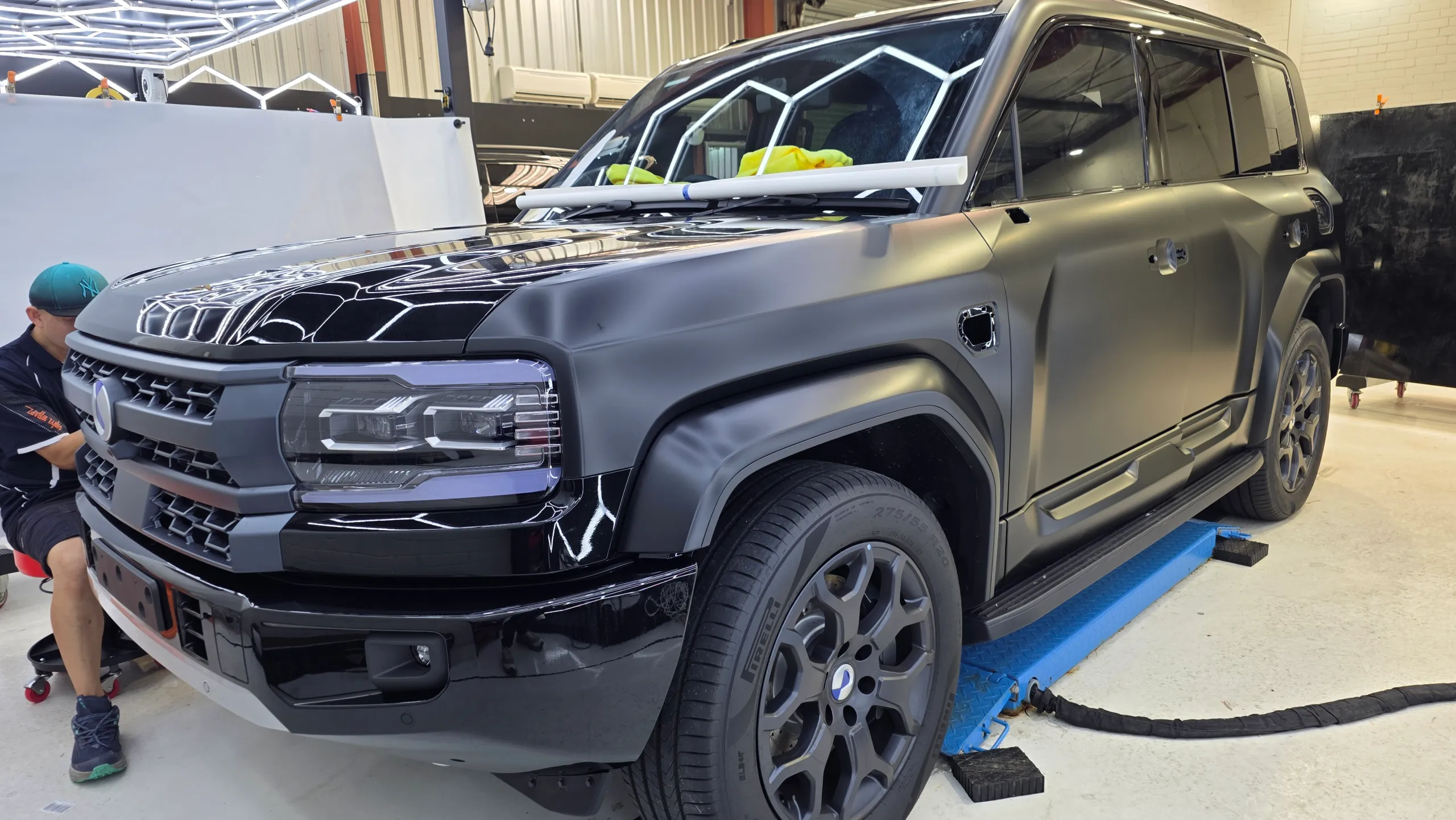 Denza B5 on a workshop lift during satin conversion, with an installer at its front bumper