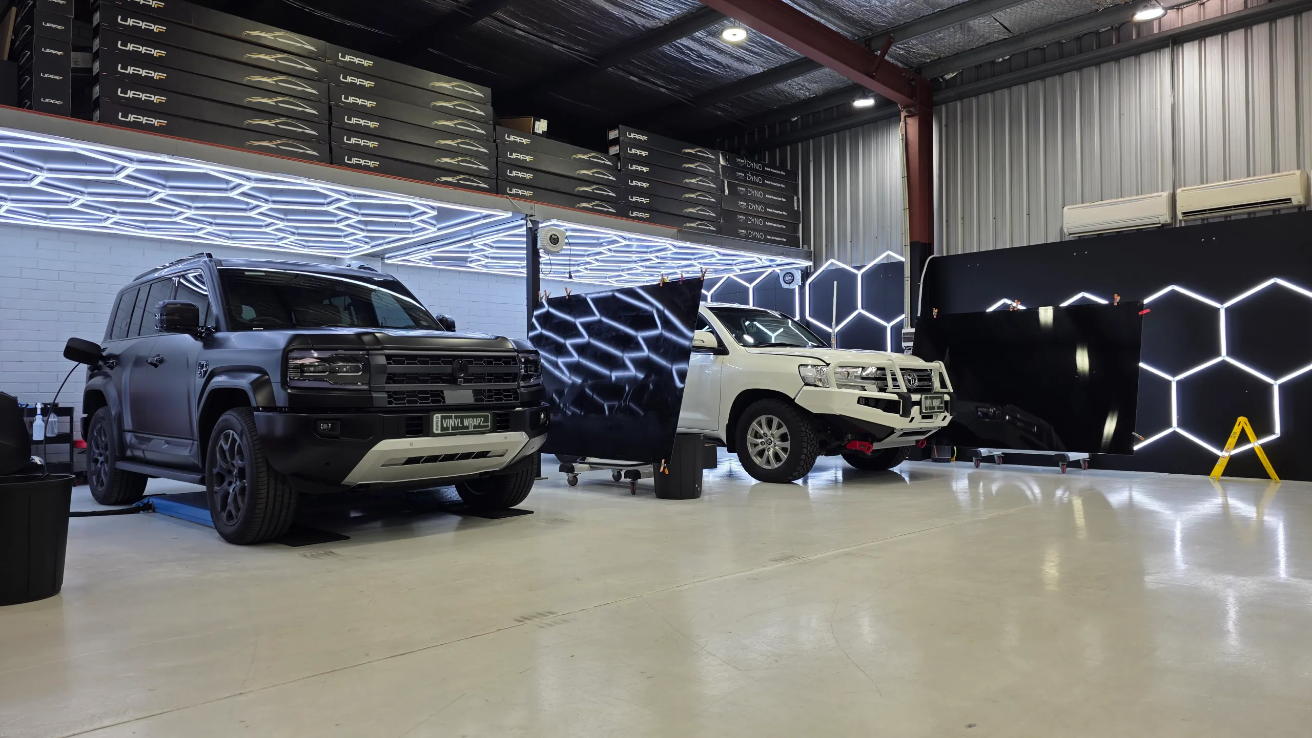Denza B5 and a white LandCruiser beneath the workshop ceiling lights and film storage shelves