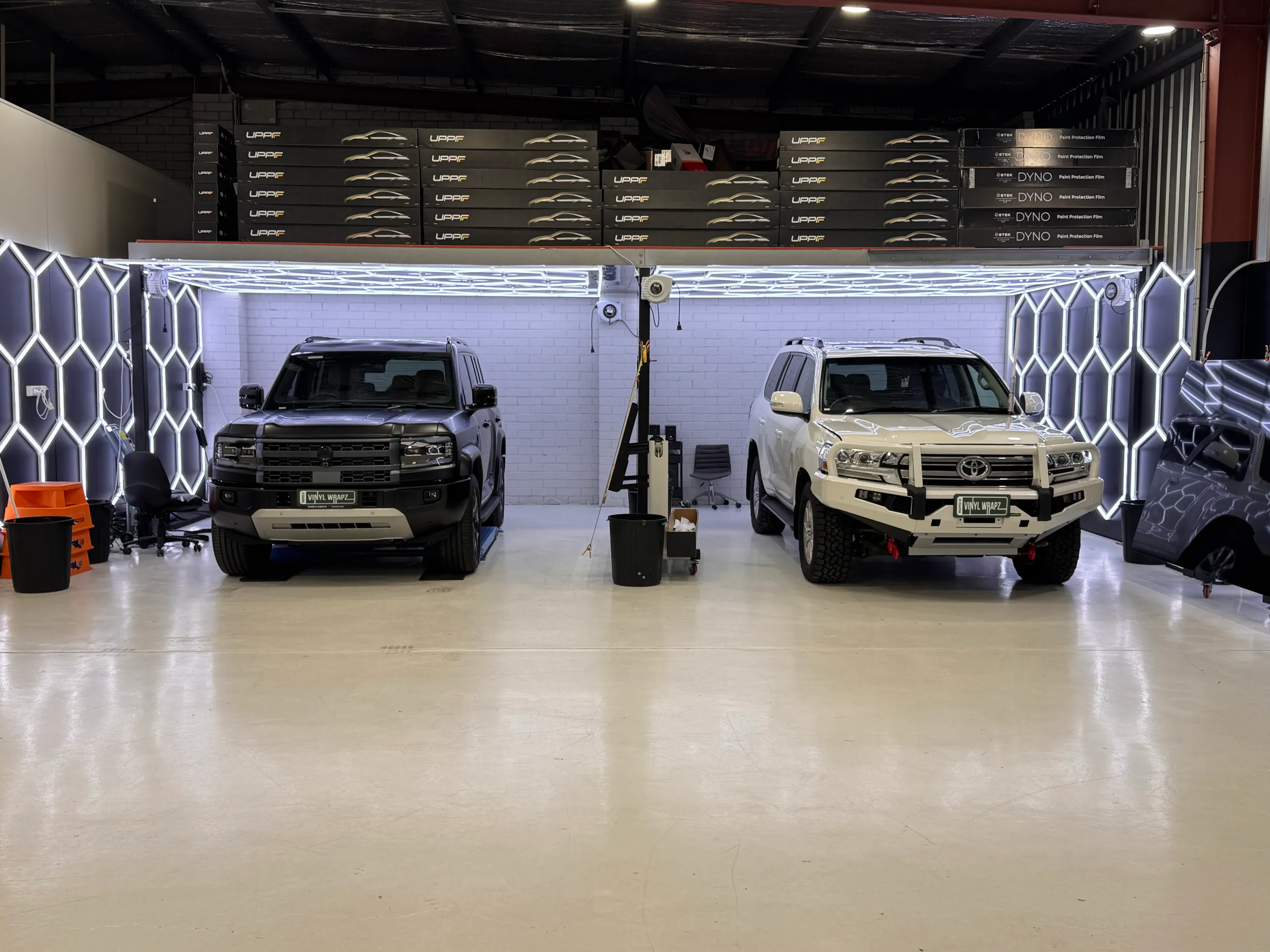 Wide workshop view of the dark Denza B5 beside a white LandCruiser under ceiling lights